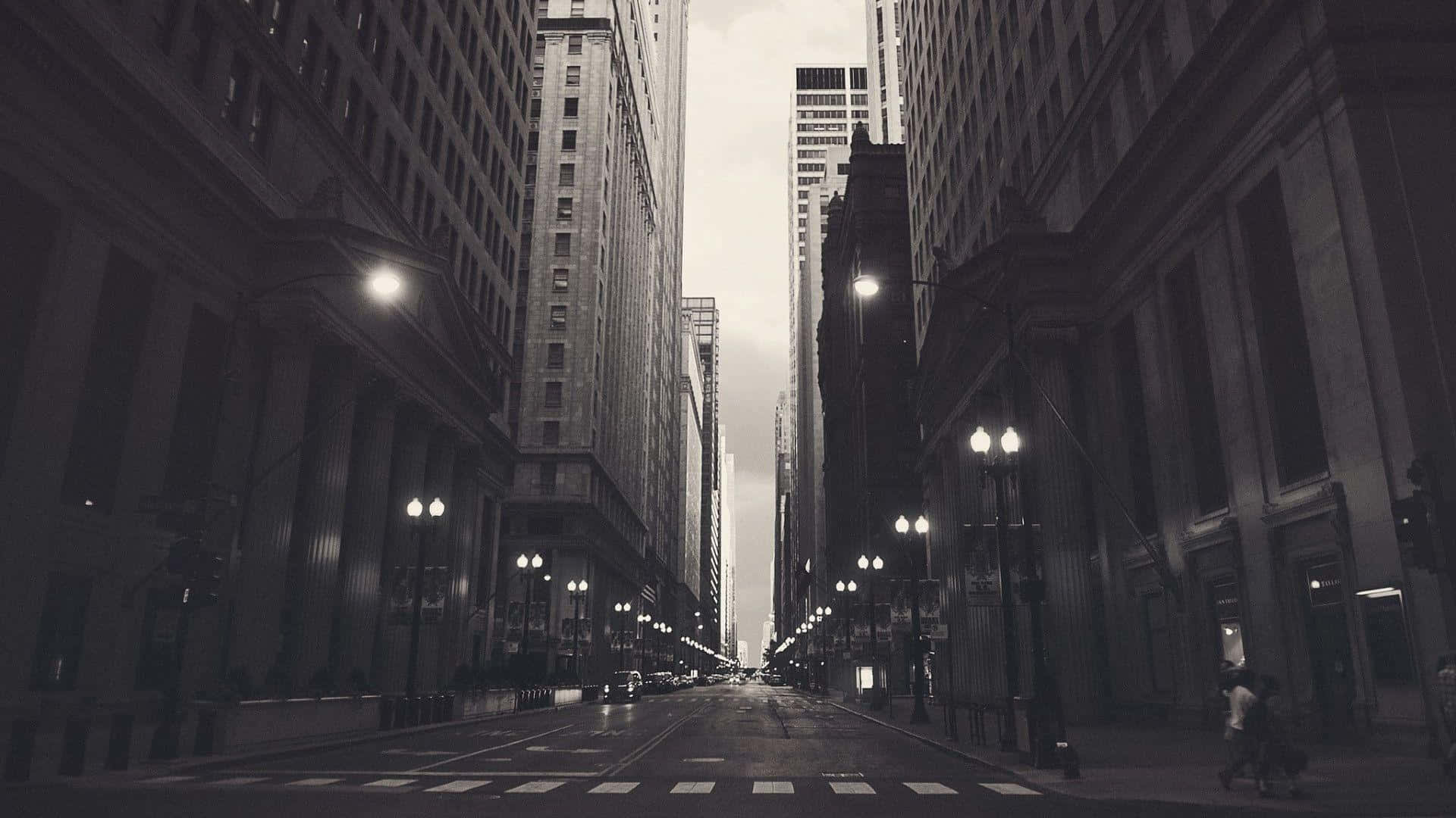 Monochrome 桌布 壁紙 — 在陰天天空下，一條濕漉漉的城市街道兩旁高聳的摩天大樓的單色景觀。