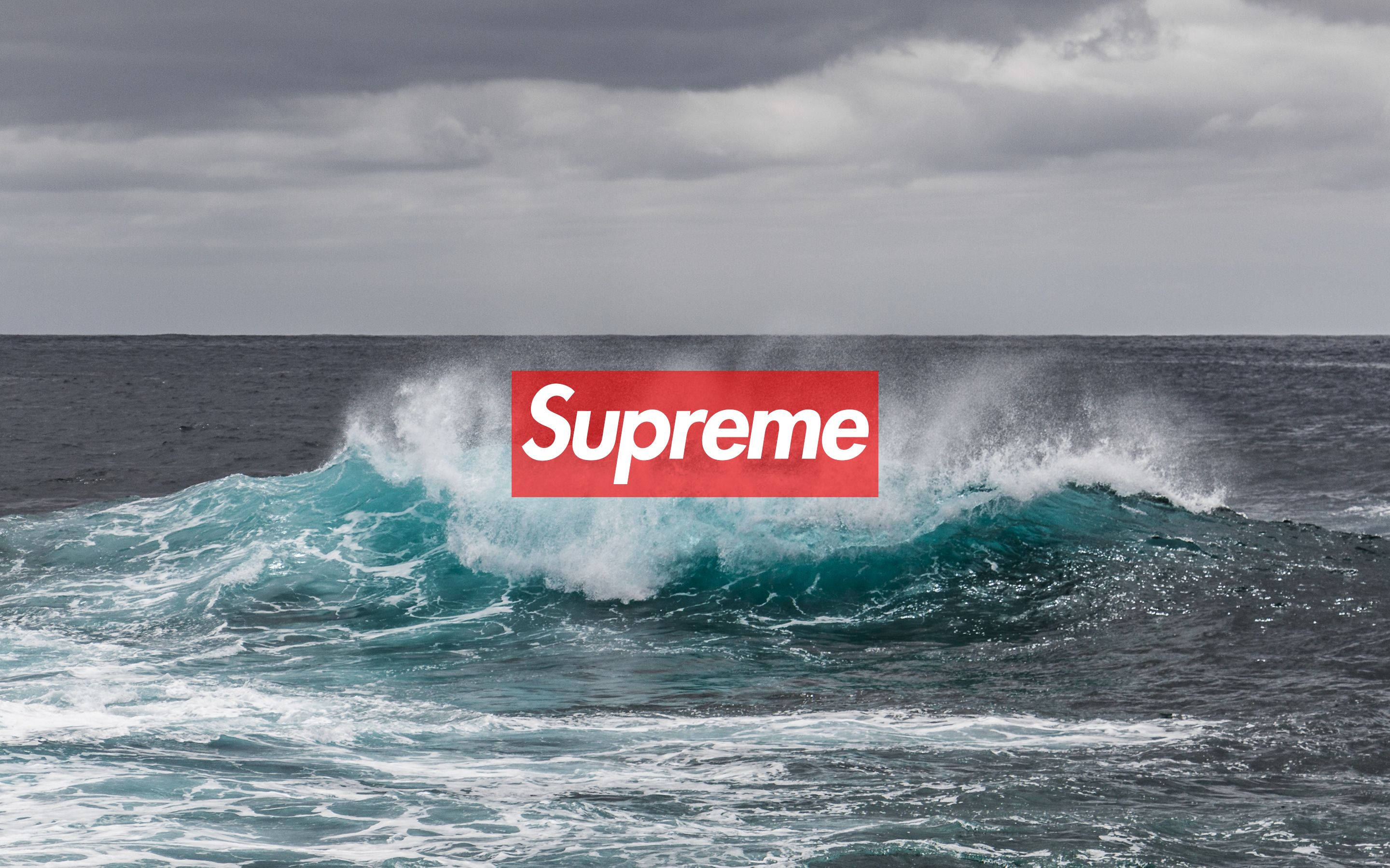 supreme 桌布 壁紙 — 在陰天天空下，一道強勁的藍綠色海浪衝擊，上面疊加了一個大膽的紅色Supreme標誌。