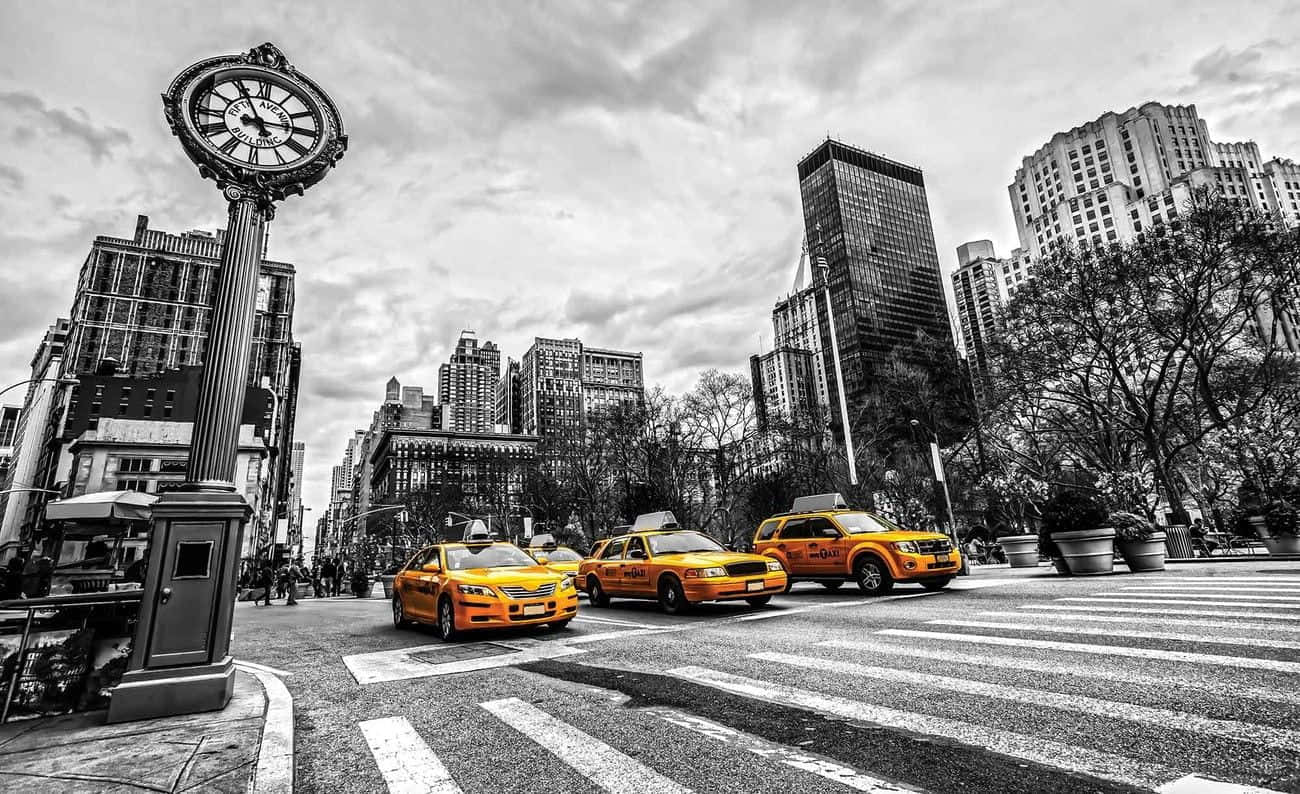 Yellow Cab 桌布 壁紙 — 在陰天天空下，鮮黃色的計程車與黑白城市景觀形成對比，城市景觀中有一座高聳的時鐘和摩天大樓。