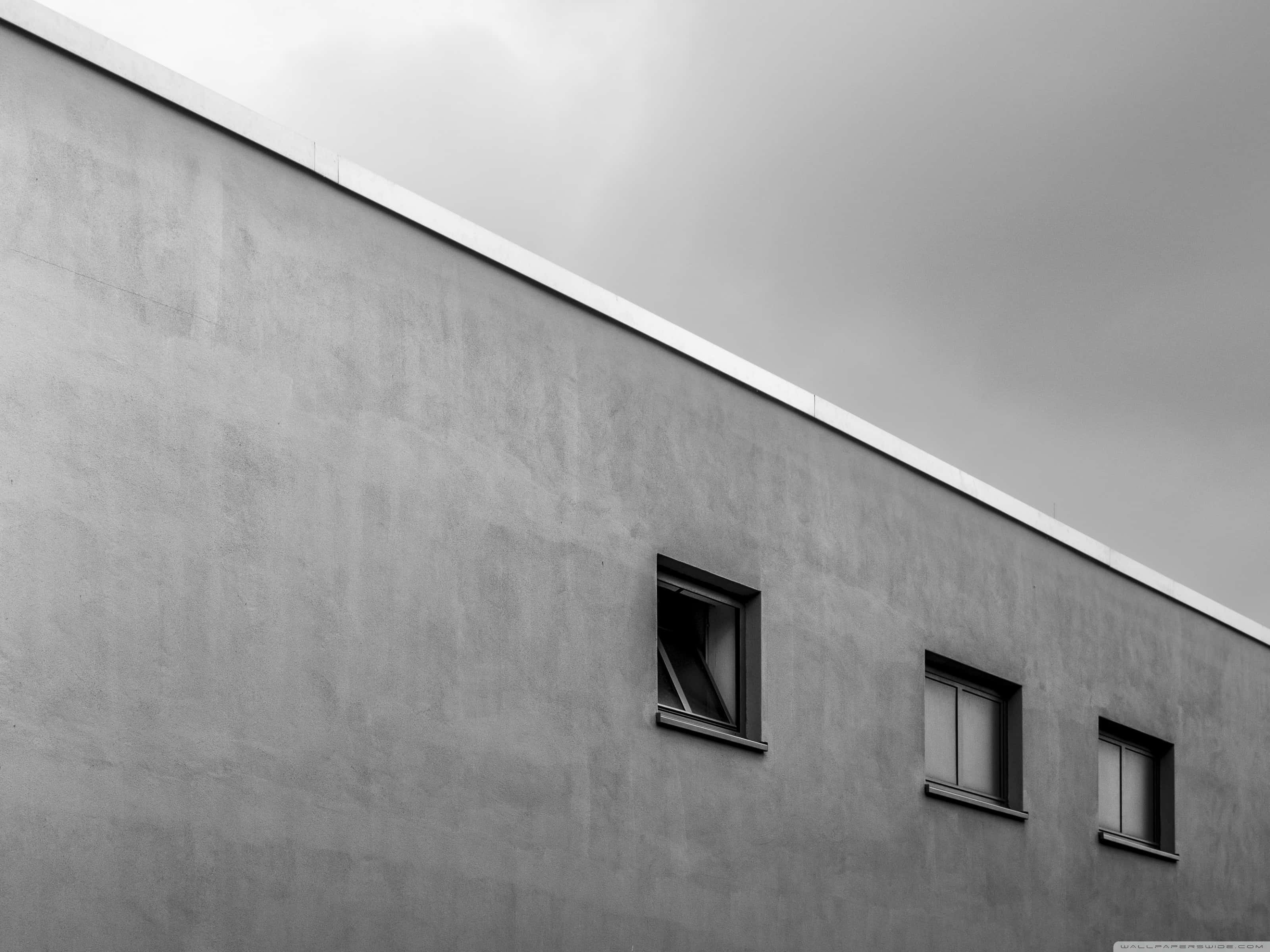 Minimalist Gray 桌布 壁紙 — 在陰天拍攝的極簡黑白建築照片，展示一座混凝土建築外牆，上有三扇小窗。