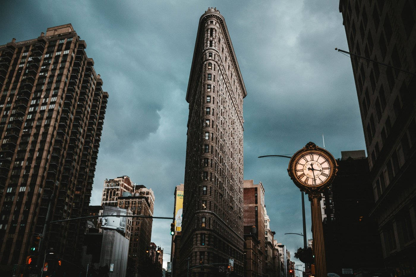 Flatiron Building 桌布 壁紙 — 在陰沉灰暗的天空下，以低角度拍攝標誌性的熨斗大廈，前景有一座復古街鐘。