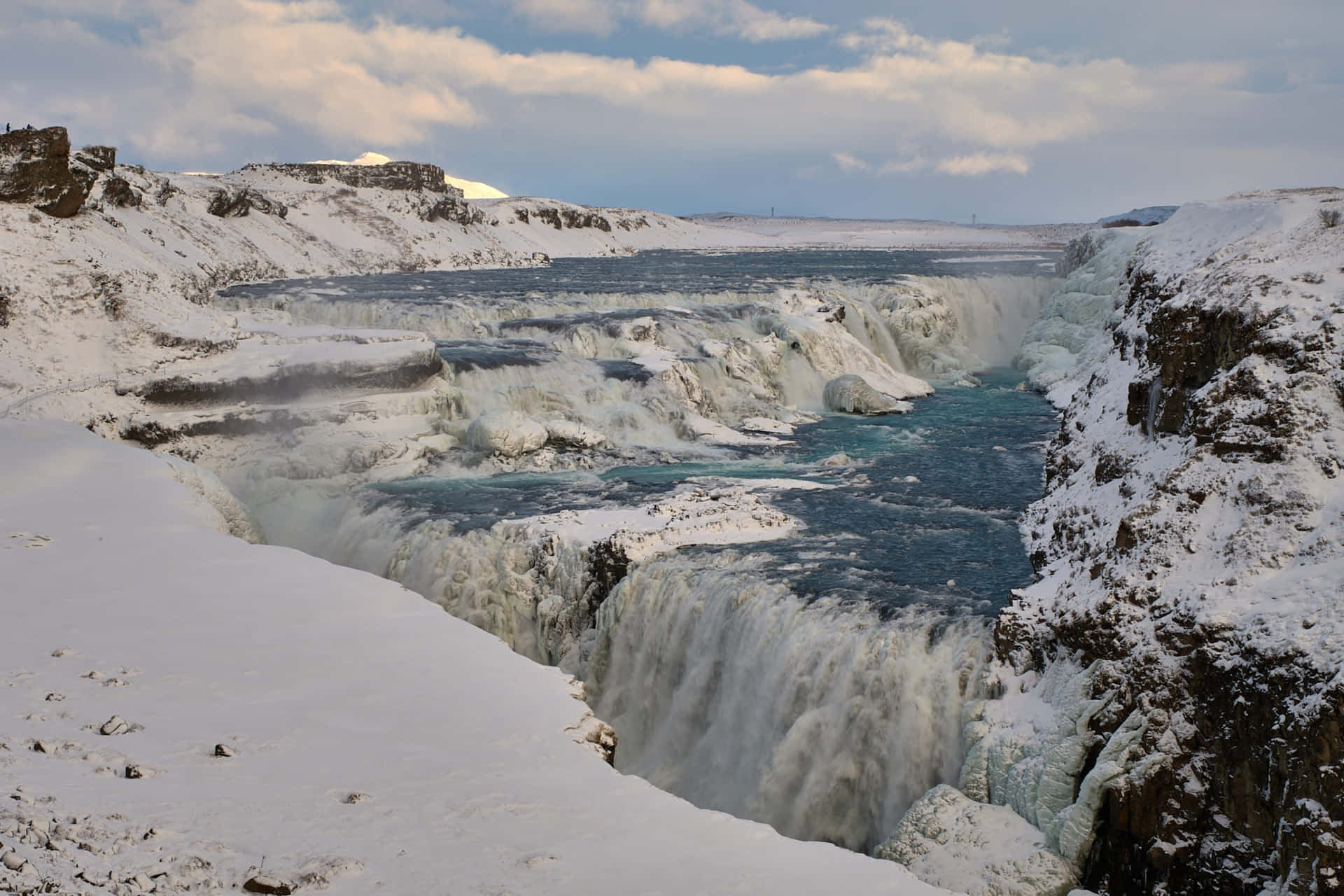 Iceland 桌布 壁紙 — 在陰沉的冬日天空下，一座雄偉的雪覆蓋瀑布強力地穿過冰崖傾瀉而下。