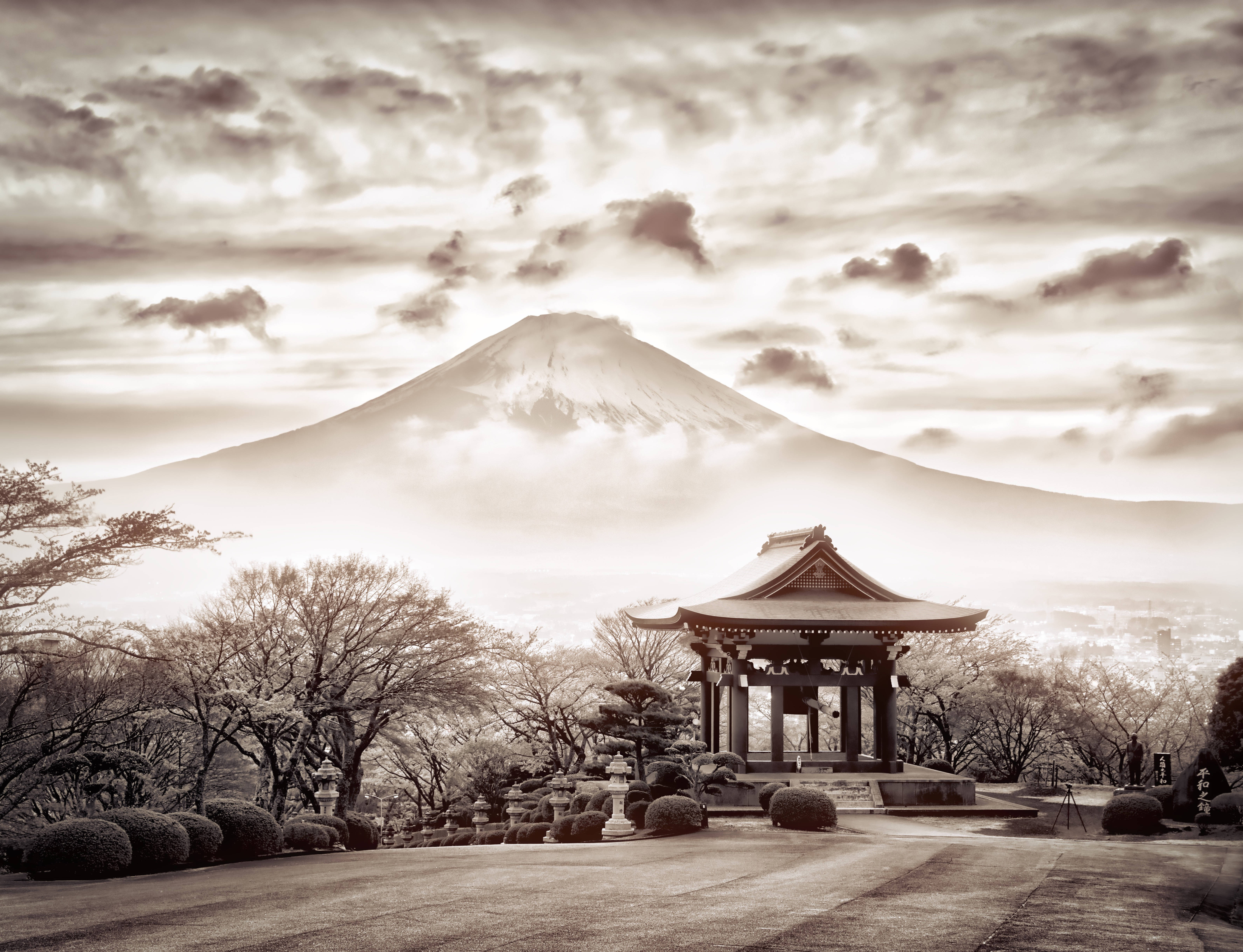 富士山 桌布 壁紙 — 在陰雲密佈的天空下，一座傳統日本亭閣後方，富士山以懷舊的棕褐色調聳立於光禿樹木和整齊灌木叢之間。