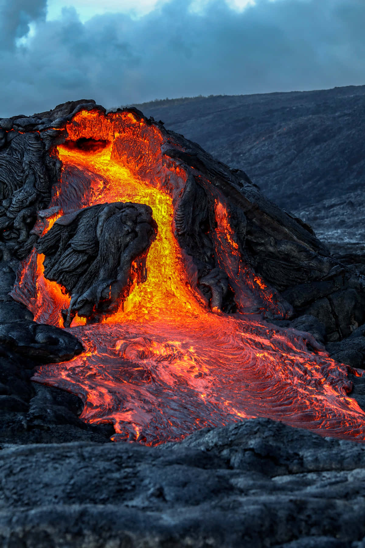 Volcano 桌布 壁紙 — 在陰鬱的暮色天空下，鮮豔的橙色熔岩沿著崎嶇的黑色火山懸崖傾瀉而下。