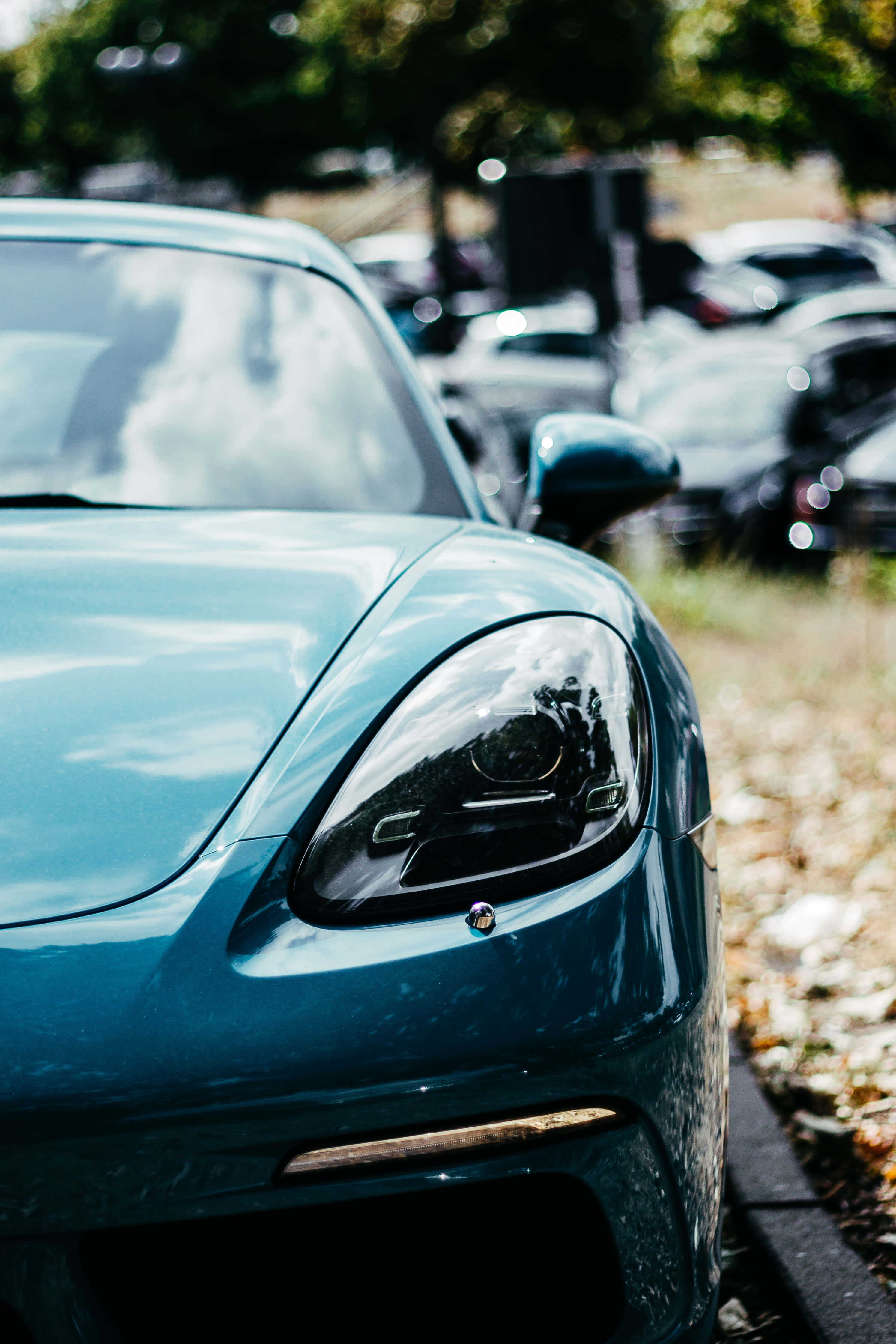 Blue Car 桌布 壁紙 — 在陽光明媚的停車場中，時尚青綠色跑車頭燈的特寫，反射出樹木和天空。