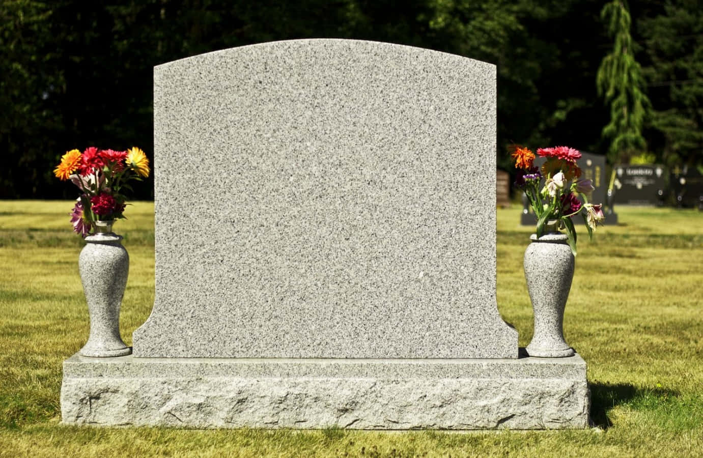 Tombstone 桌布 壁紙 — 在陽光明媚的墓地中，一座莊嚴的花崗岩墓碑兩側擺放著鮮豔的花瓶。