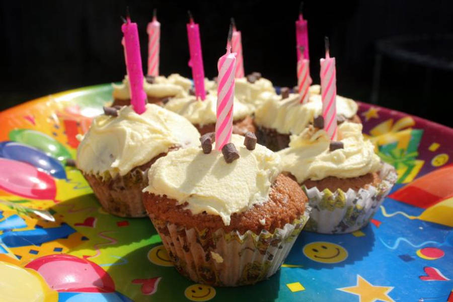 Birthday 桌布 壁紙 — 在陽光明媚的日光下，色彩繽紛的派對盤上放著明亮照亮的杯子蛋糕，上面有粉紅色蠟燭和巧克力碎片。