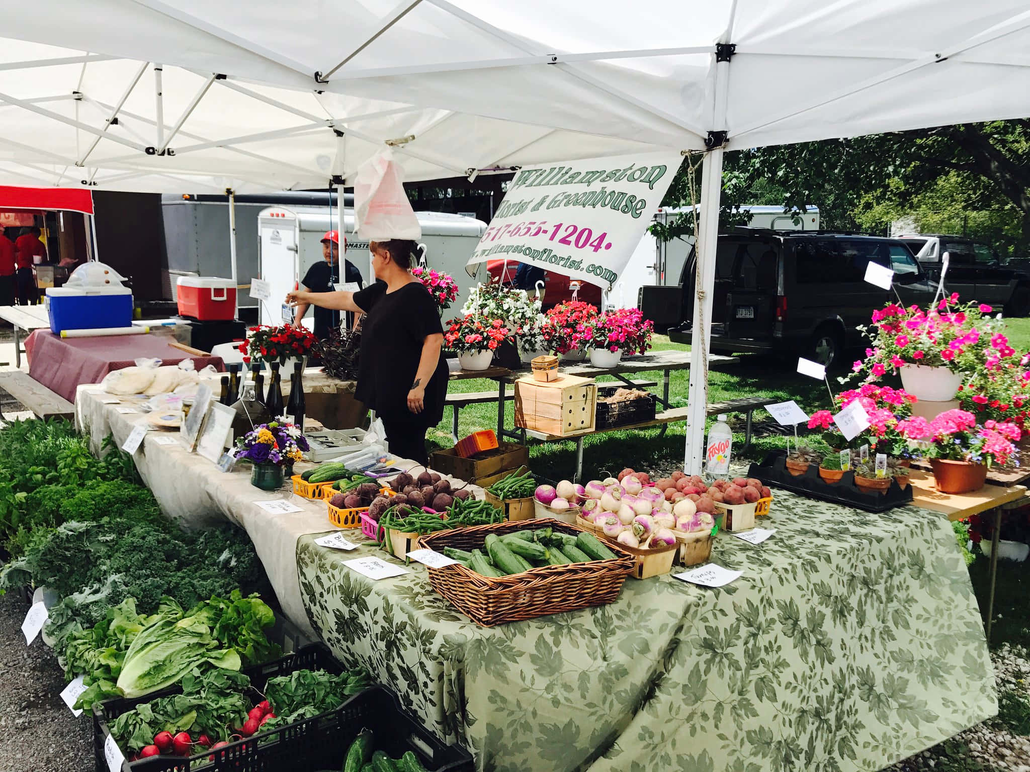 Farmers Market 桌布 壁紙 — 在陽光明媚的日子裡，一個充滿活力的戶外農貿市場攤位在白色遮陽篷下展示新鮮農產品和色彩繽紛的鮮花。