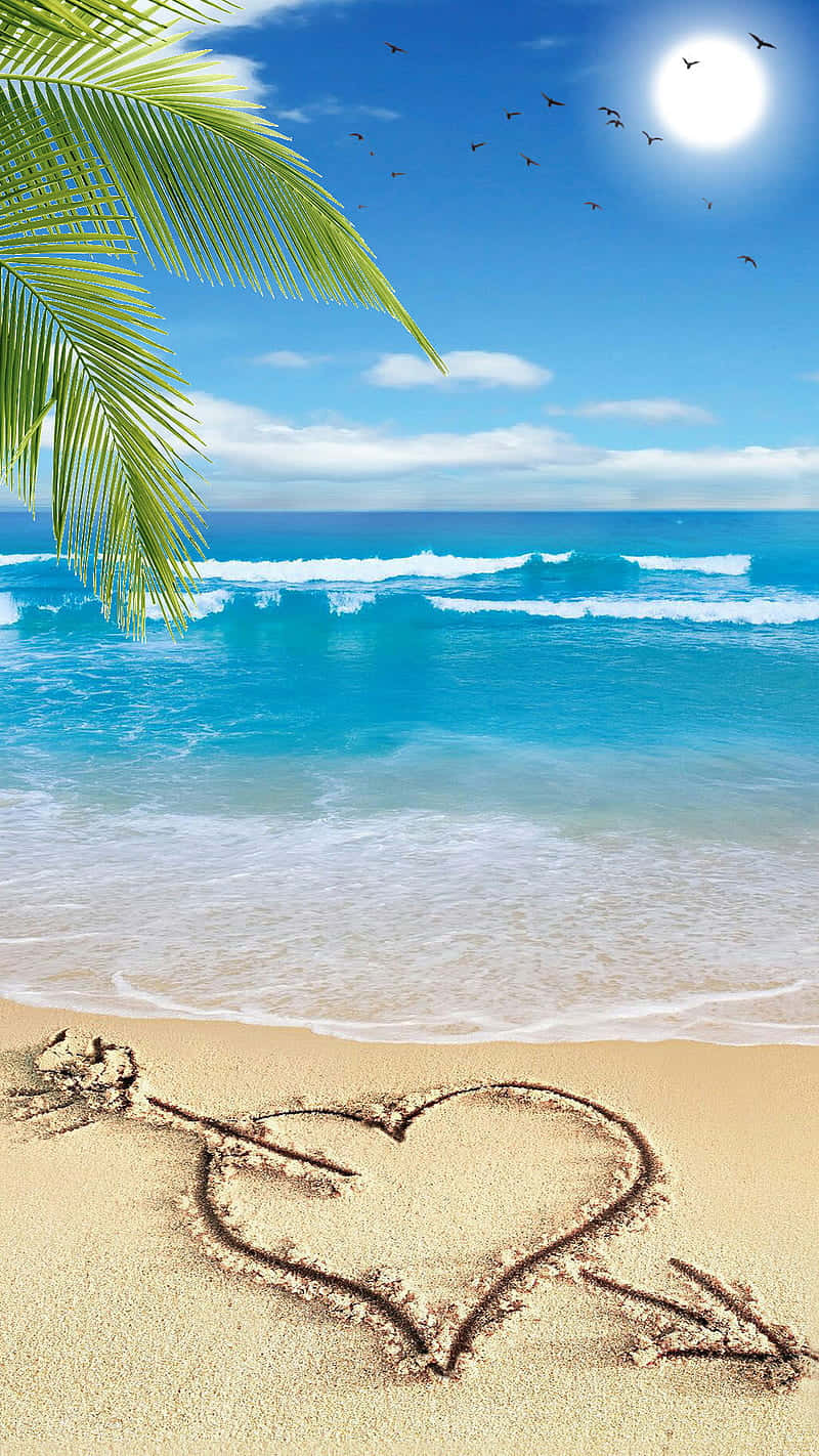 Beach Love 桌布 壁紙 — 在陽光明媚的海灘上，用沙畫出的一顆心，伴隨著碧綠的海浪、棕櫚葉和鳥兒在明亮的太陽下飛翔。