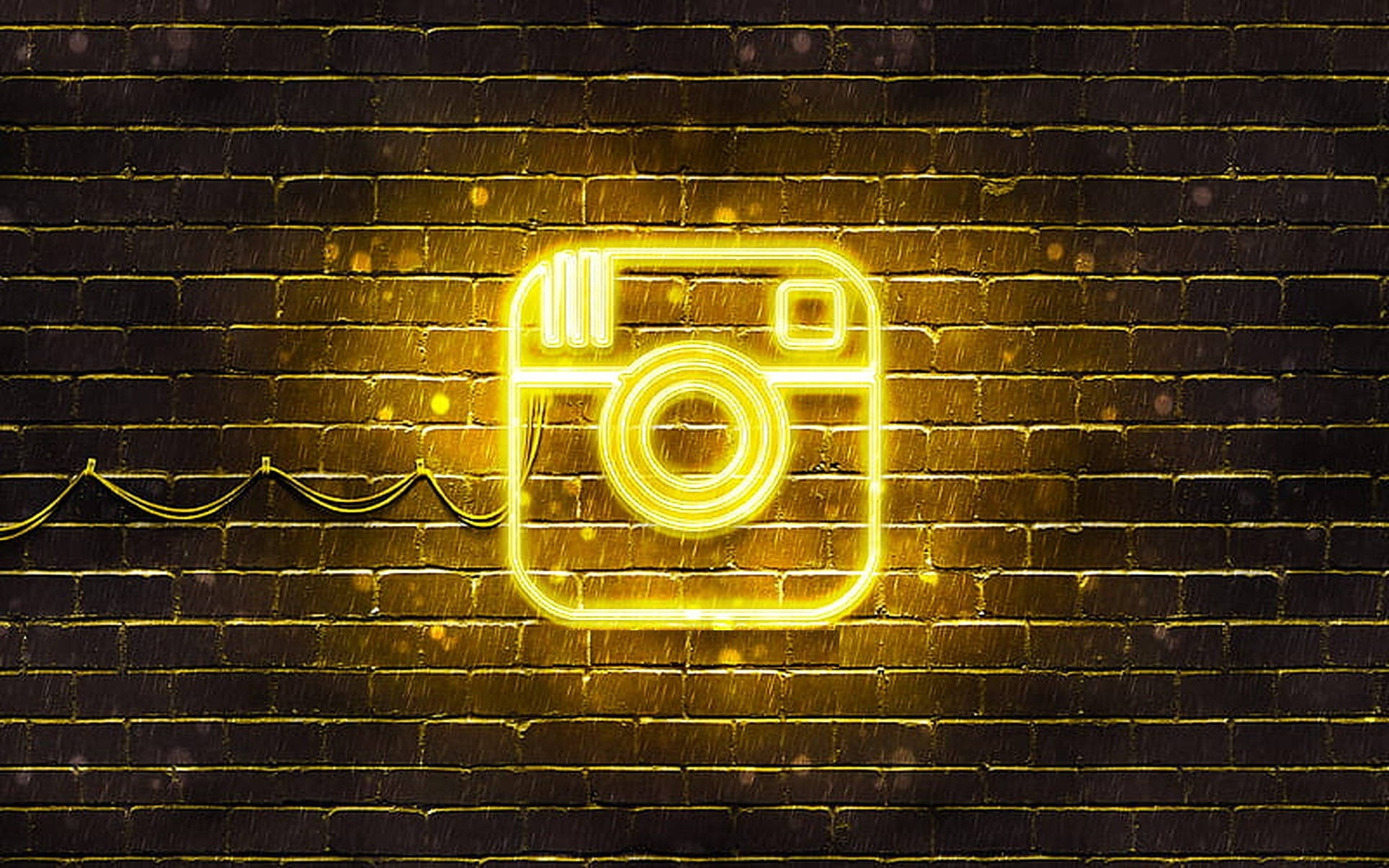 Instagram 桌布 壁紙 — 在雨中安裝在深色磚牆上的發光黃色霓虹燈Instagram標誌招牌。