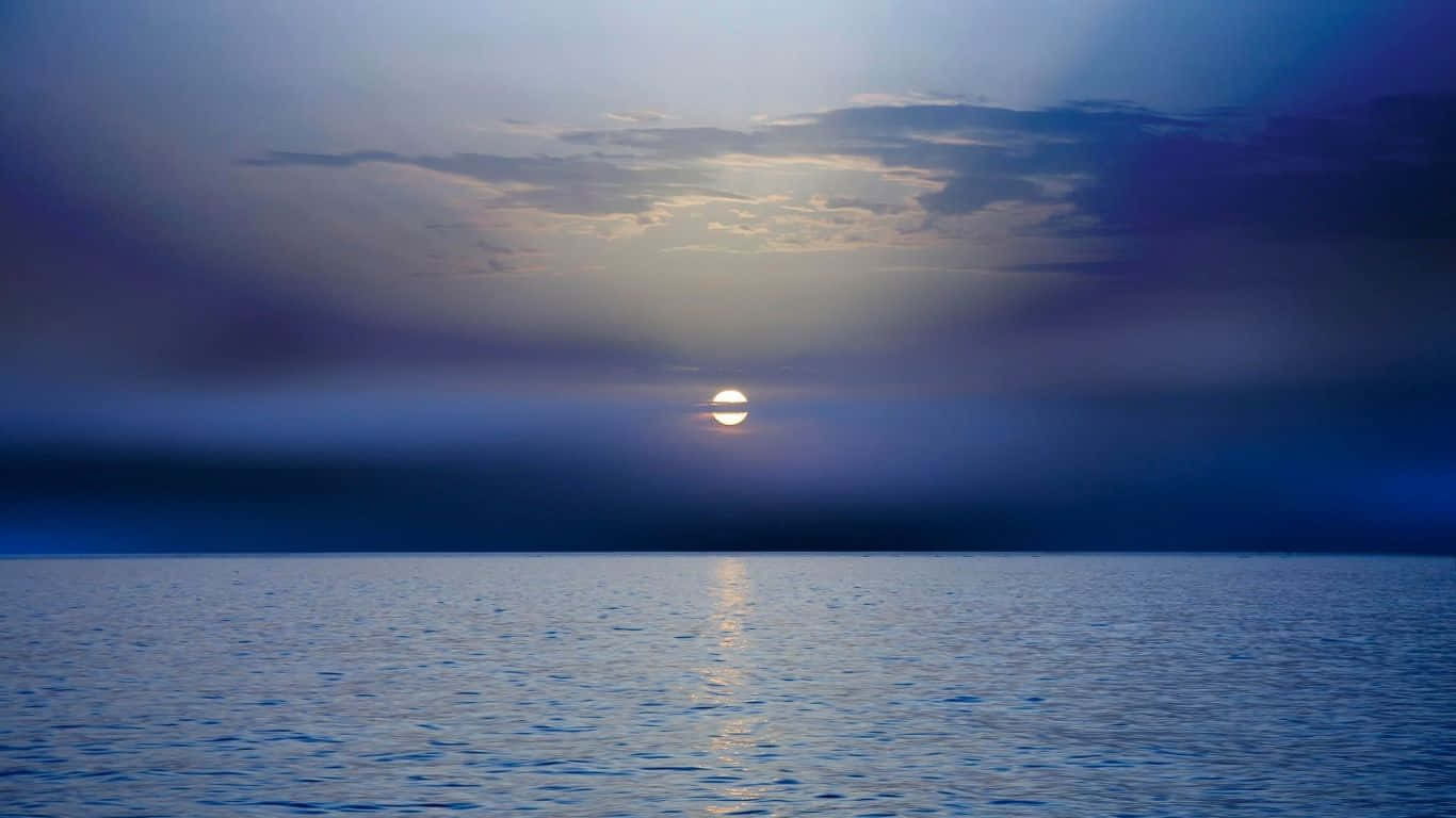 Laptop 1366 X 768 桌布 壁紙 — 在雲層密佈的天空下，夕陽在平靜的海洋上投射出一條金色的小徑，橫跨深藍色的海水。