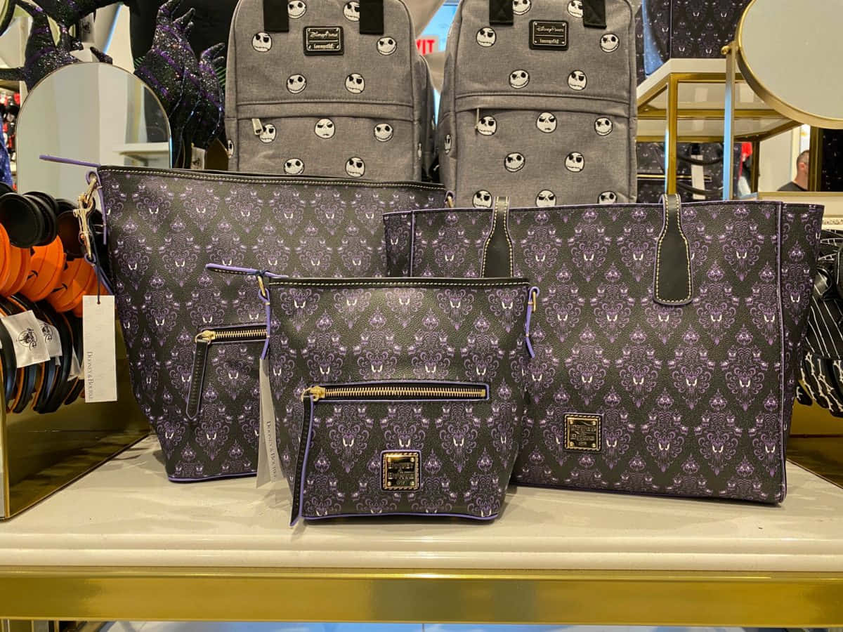 Haunted Mansion 桌布 壁紙 — 在零售店的鍍金邊櫃檯上展示的紫色和黑色 Jack Skellington 圖案 Dooney & Bourke 手提包。