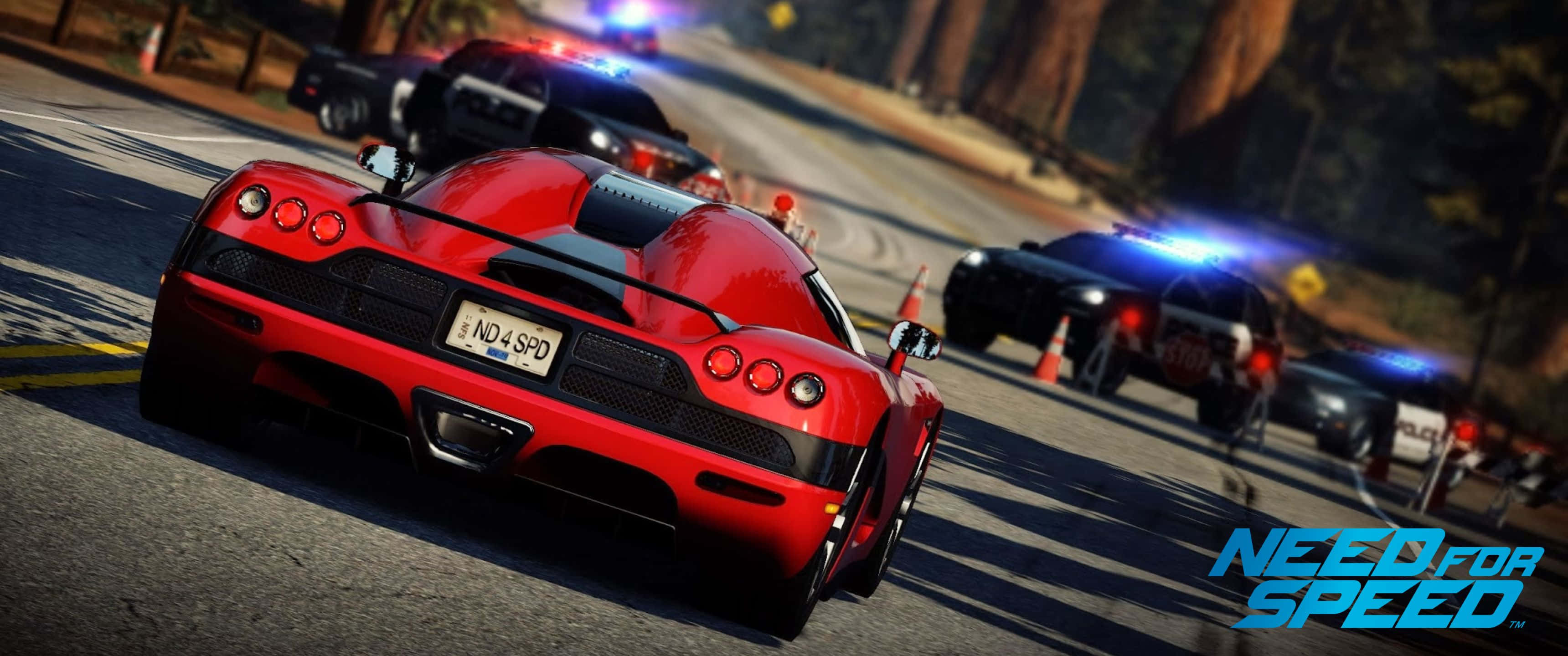 3440x1440p Need For Speed 桌布 壁紙 — 在電子遊戲場景中，一輛紅色跑車在森林道路上飛馳，被閃著警燈的警車追趕。
