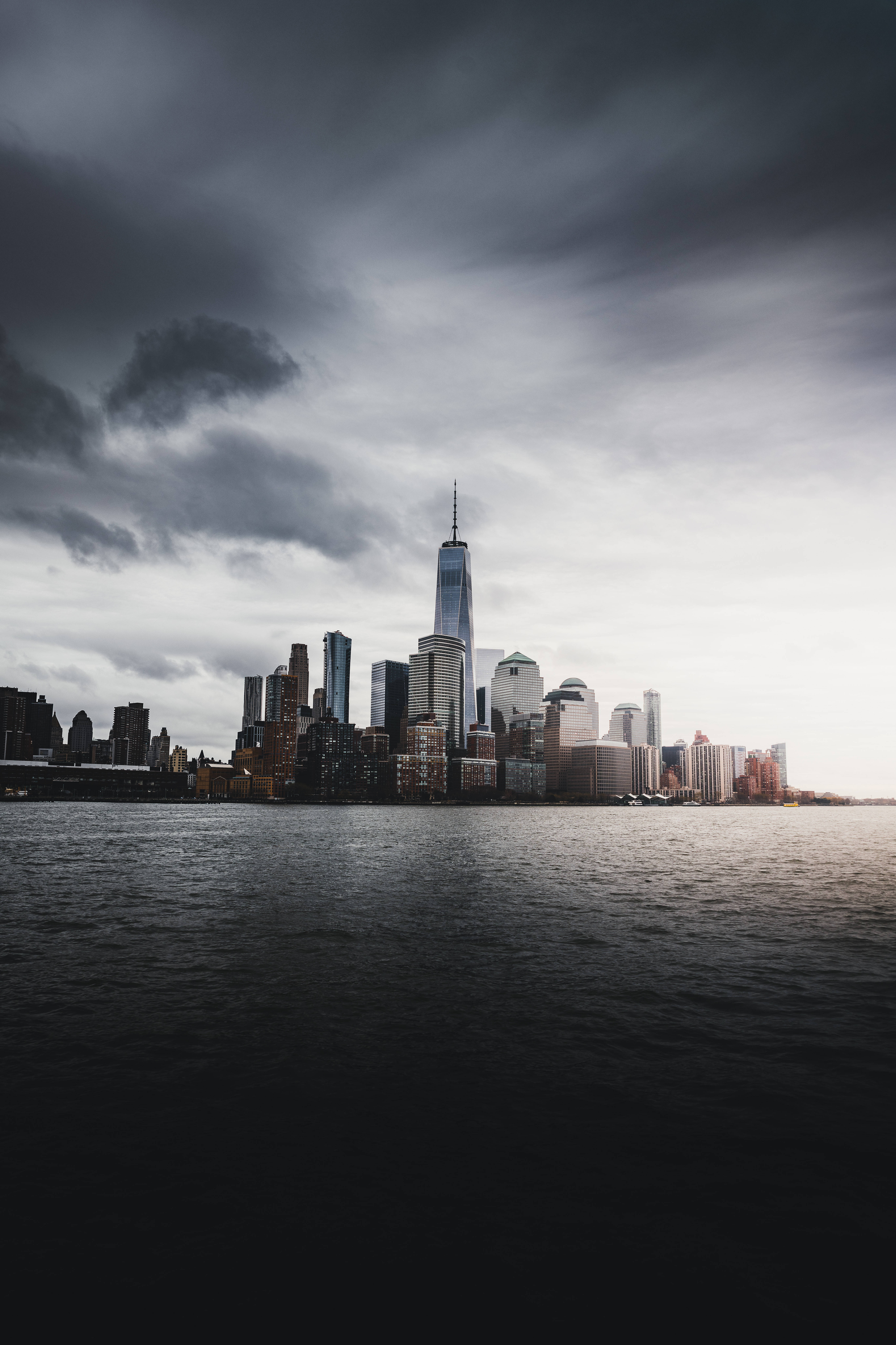 Skyscraper 桌布 壁紙 — 在風暴般的灰色天空下，摩天大樓從黑暗的水面升起，營造出陰鬱的城市天際線。