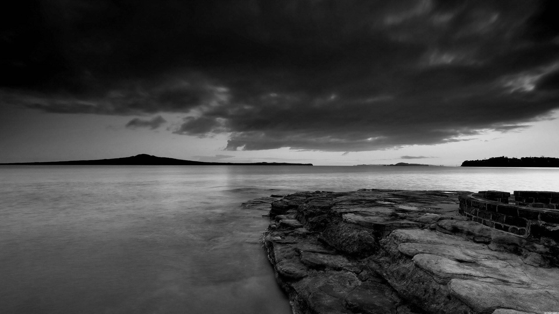 Calming 桌布 壁紙 — 在黃昏時分，戲劇性的暴風雲下，岩石海岸線的陰鬱黑白長時間曝光。
