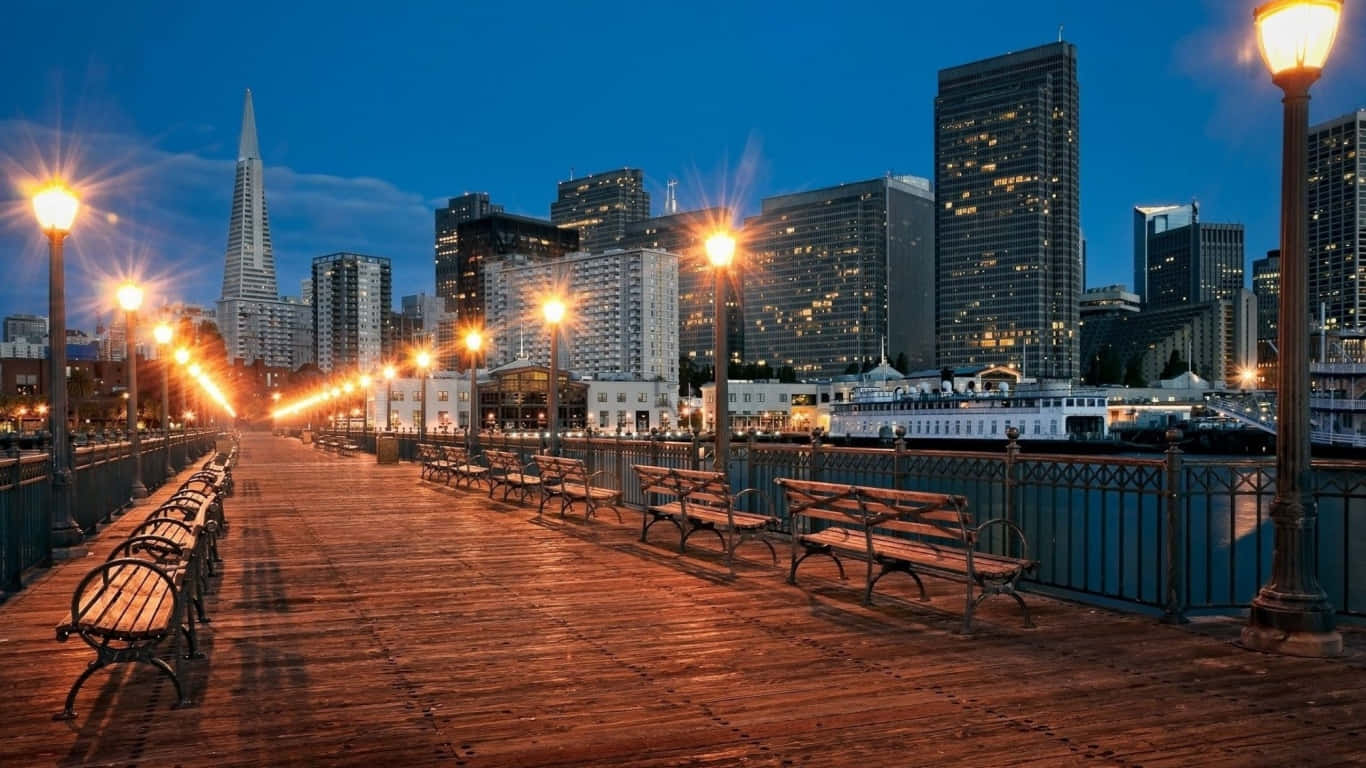 1366x768 San Francisco 桌布 壁紙 — 在黃昏時分，溫暖照明的木製碼頭，發光的街燈，背景是包含泛美金字塔的城市天際線。