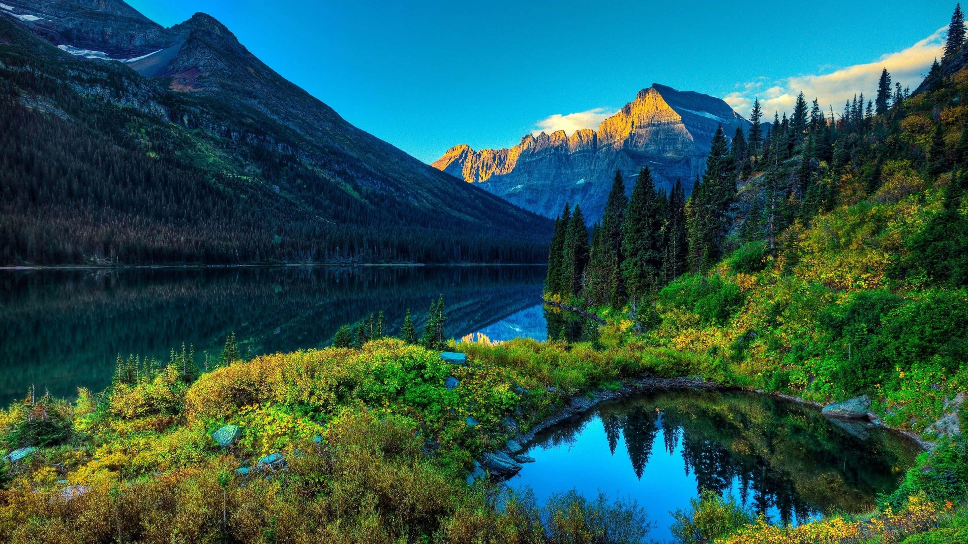 4K Ultra HD Landscape 桌布 壁紙 — 在黃金時段清澈的藍天下，寧靜的山中湖泊倒映著高聳的山峰和常綠森林。