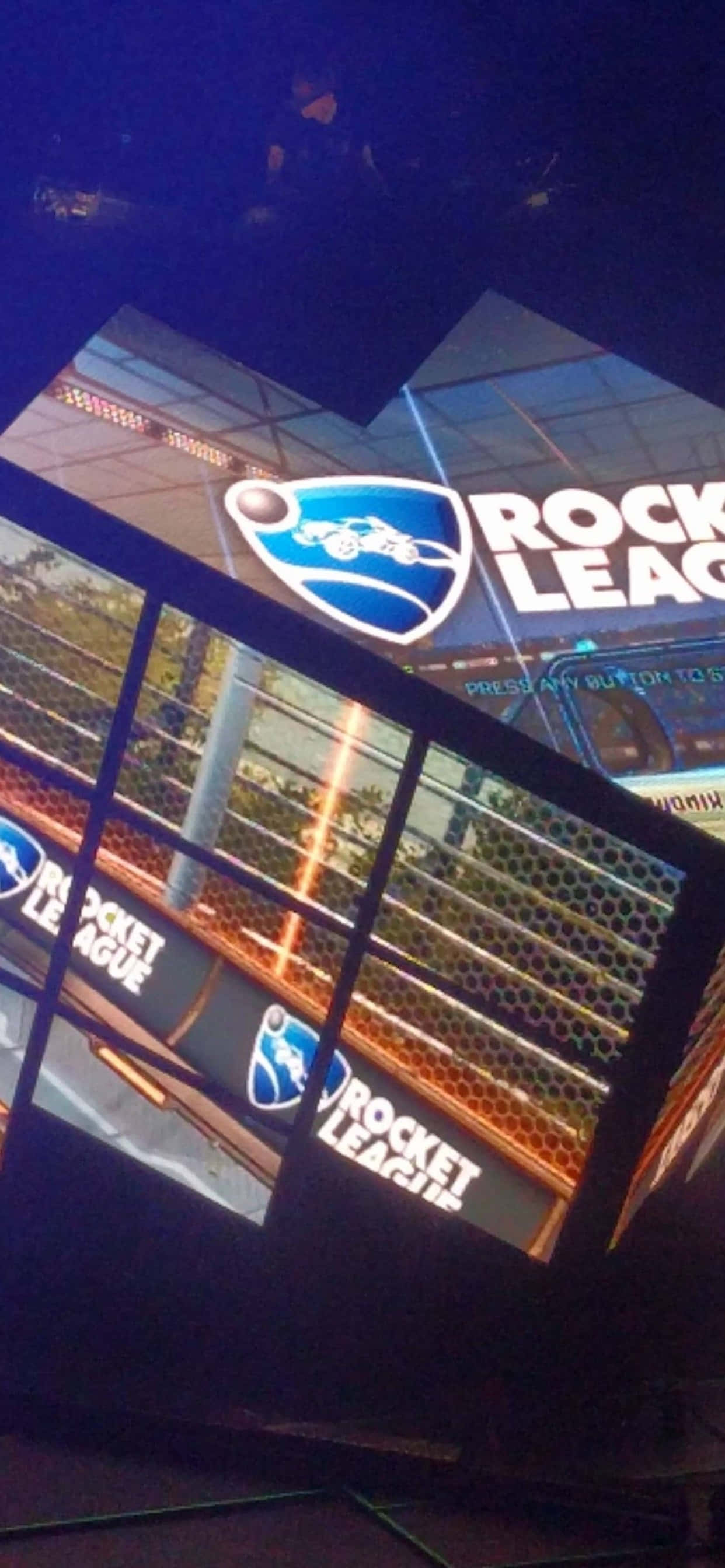 iPhone Xs Max Rocket League 桌布 壁紙 — 在黑暗場地中，帶有鮮豔藍色和橙色燈光的大型傾斜螢幕上顯示發光的Rocket League標誌。
