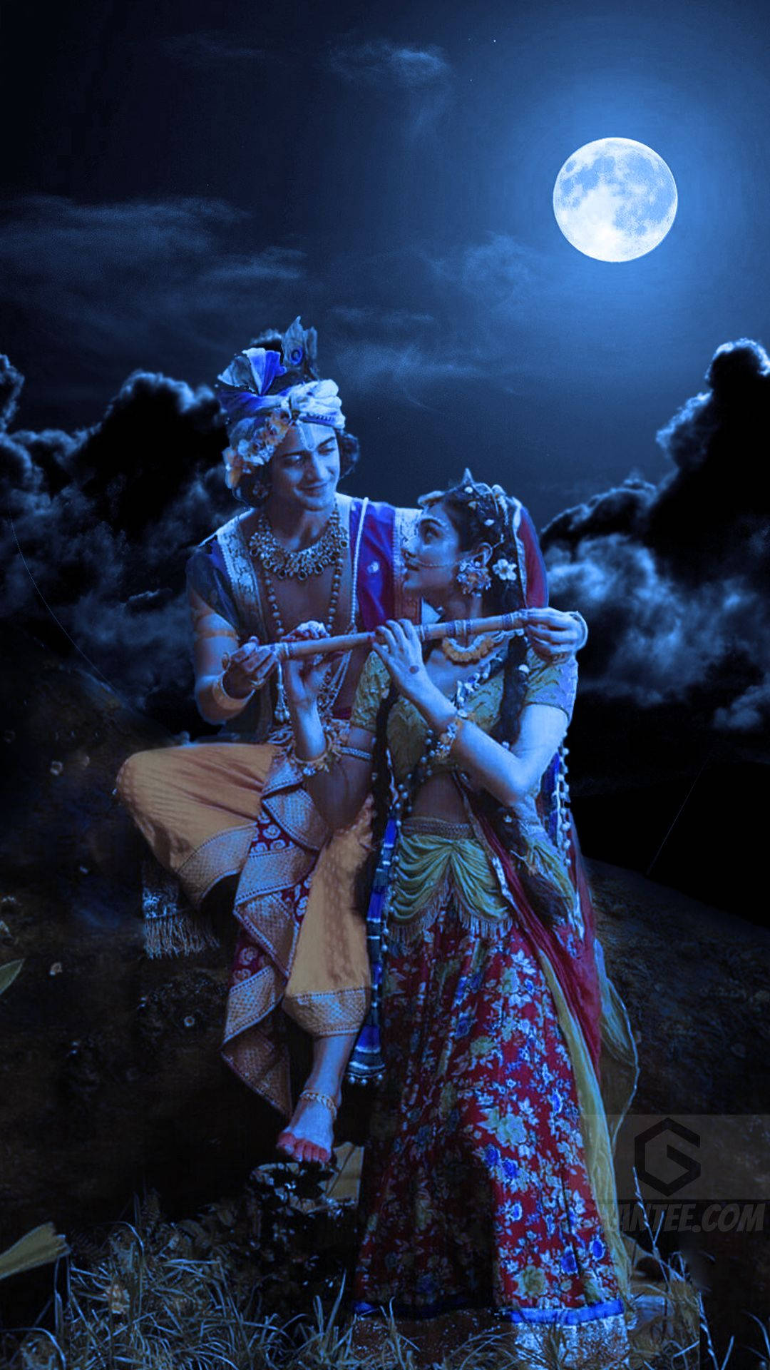 radha krishna serial 桌布 壁紙 — 在黑暗多雲的夜空下，一對穿著華麗傳統服飾的男女在閃爍的滿月下共享一支笛子。