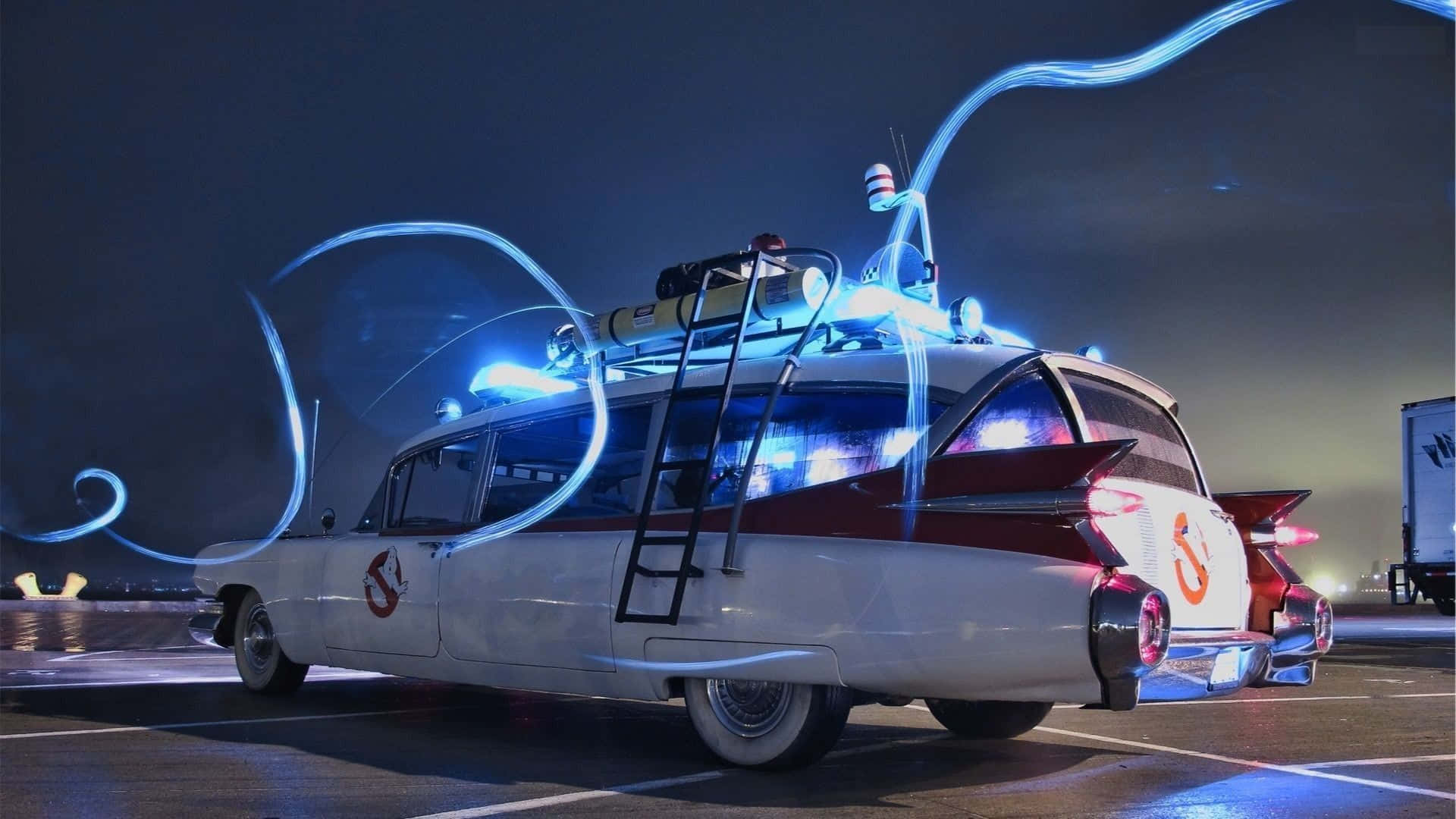 魔鬼剋星 桌布 壁紙 — 在黑暗夜空下的停車場中，Ghostbusters Ecto 1 汽車散發出藍色能量軌跡。