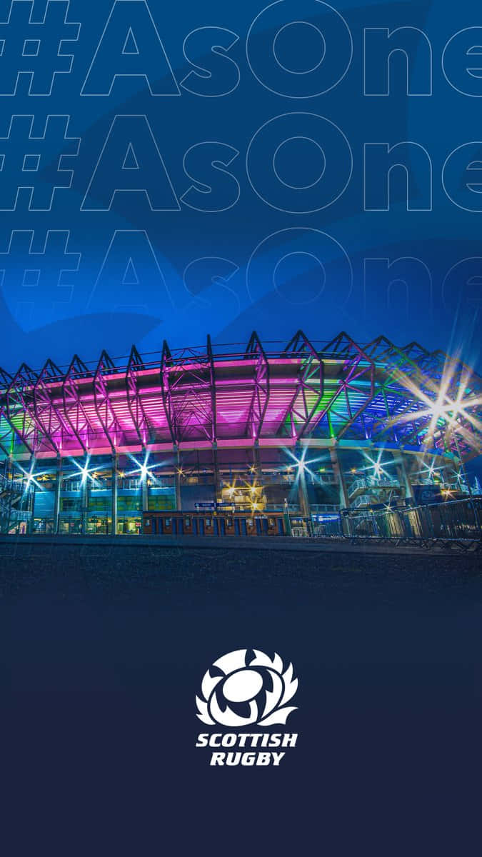 Scotland Rugby 桌布 壁紙 — 在黑暗天空下，一個現代橄欖球場被粉紅色、藍色和綠色燈光照亮的充滿活力的夜景。