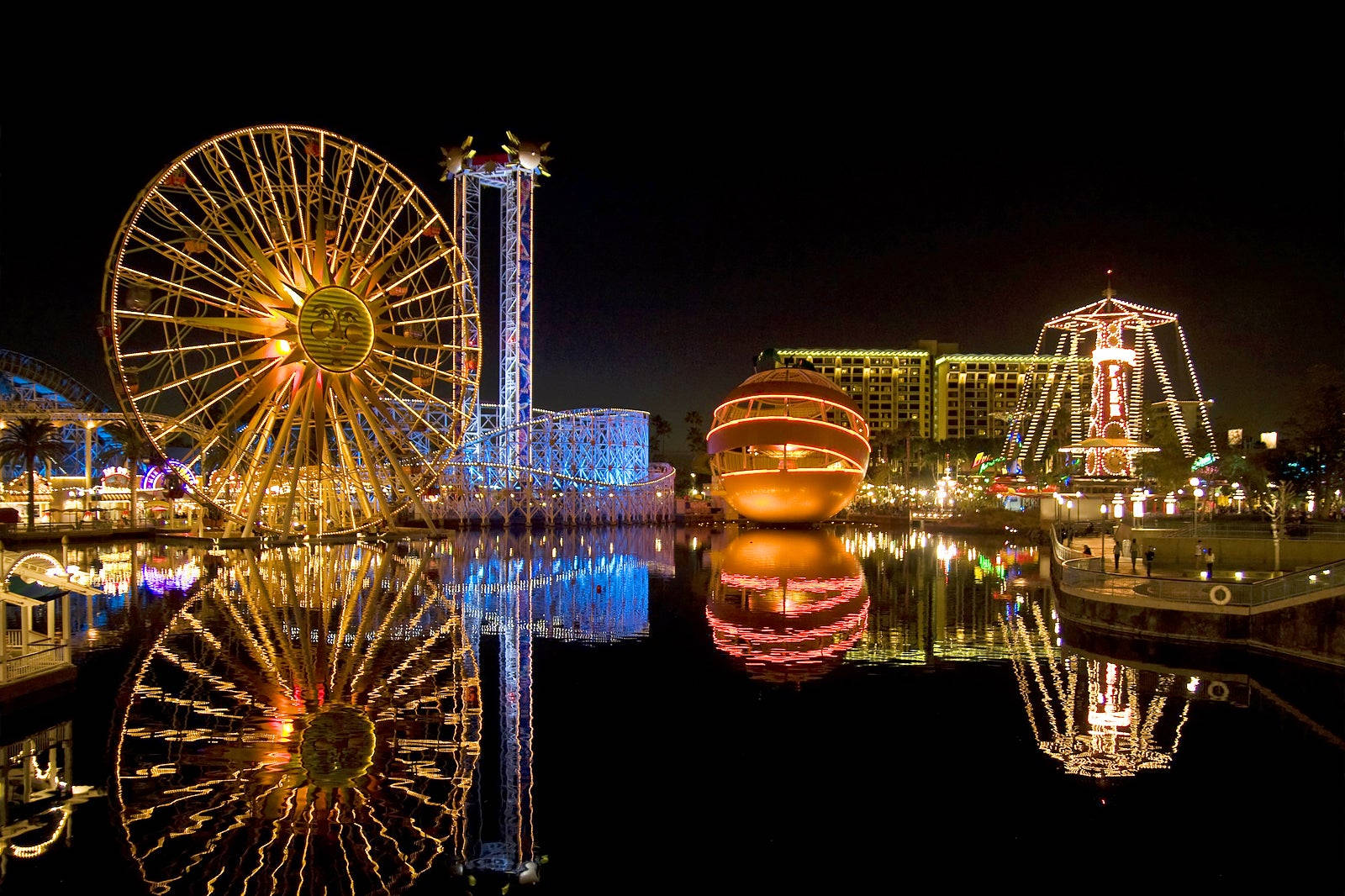 Night Aesthetic 桌布 壁紙 — 在黑暗天空下，一個耀眼的夜間遊樂園，發光的遊樂設施倒映在平靜的水面上。