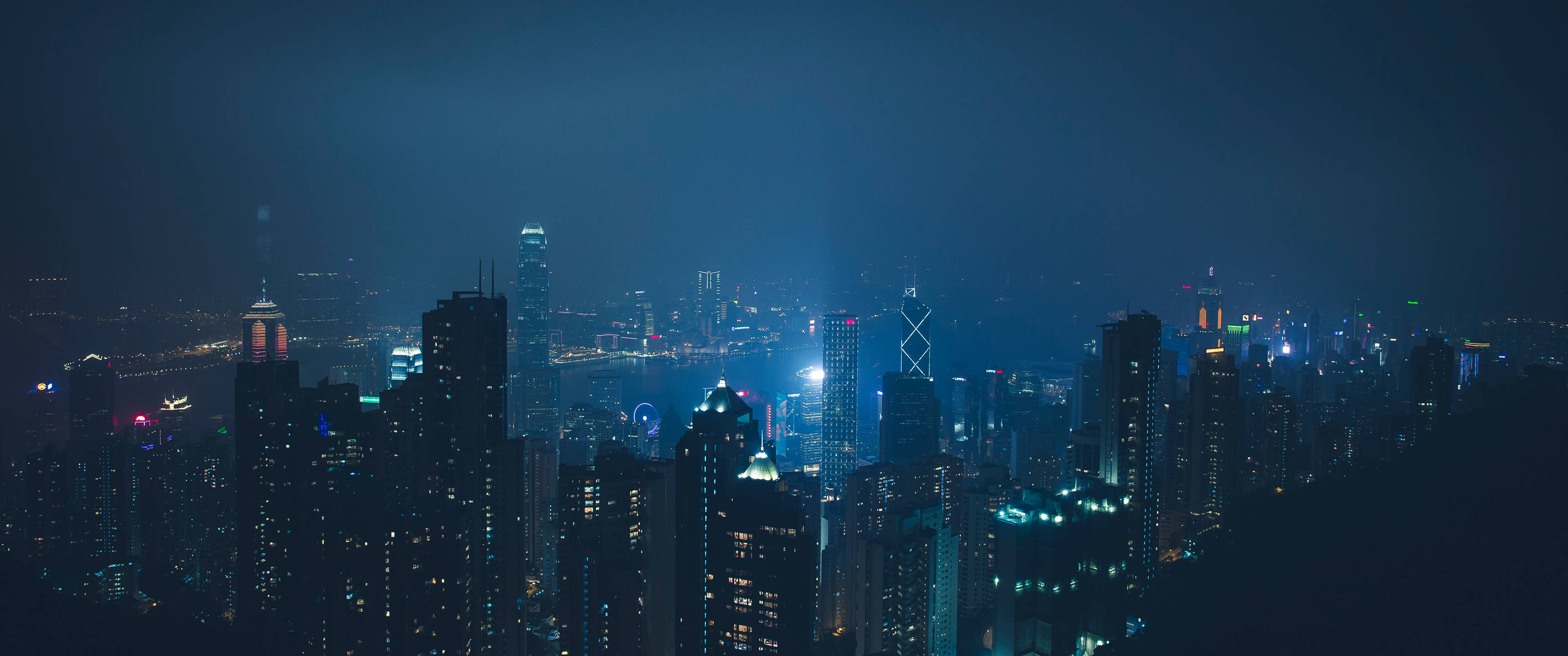 桌布 壁紙 — 在黑暗天空下，密集的城市景觀中高聳的摩天大樓閃爍著藍色和白色燈光的全景夜景。