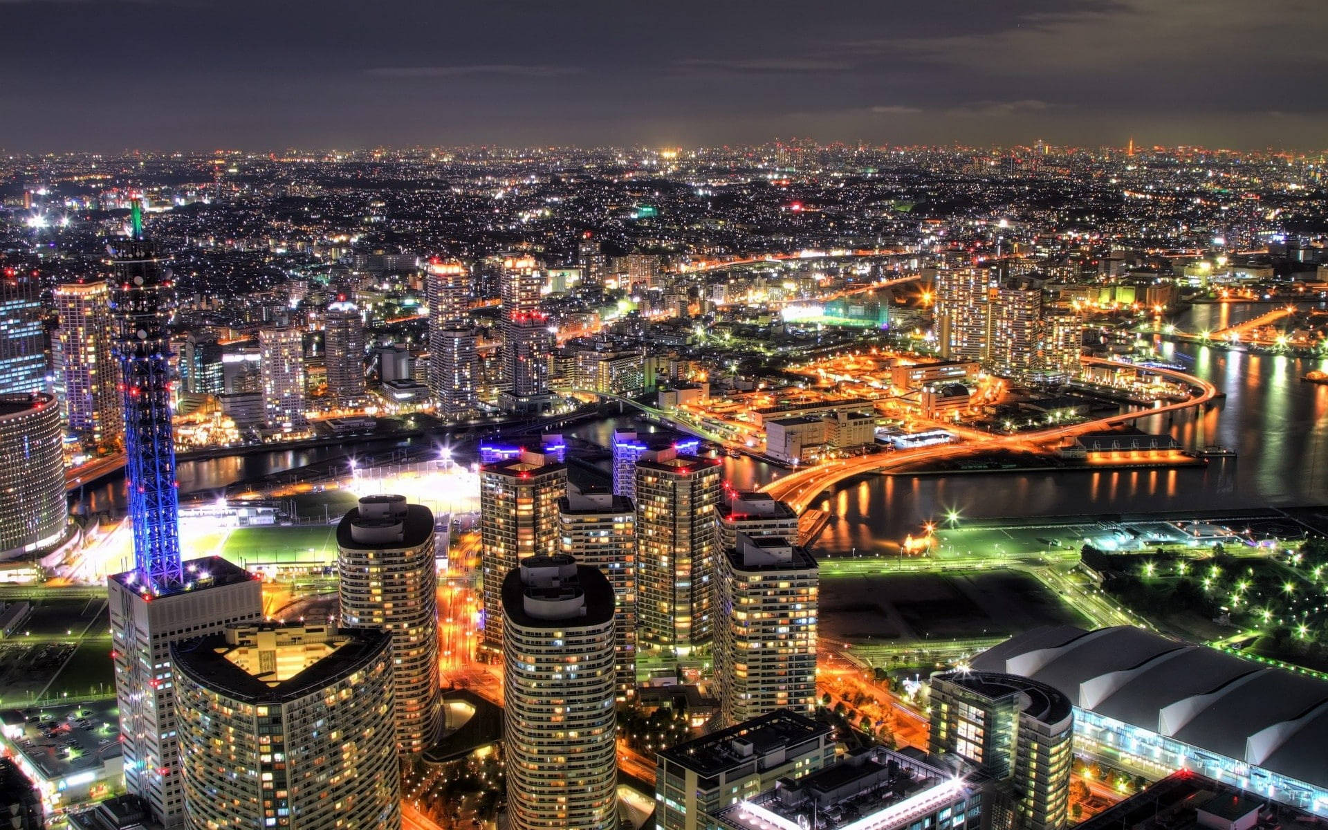 Yokohama 桌布 壁紙 — 在黑暗天空下，廣闊城市景觀的夜間航拍，閃爍的摩天大樓、河流和橋樑被照亮。