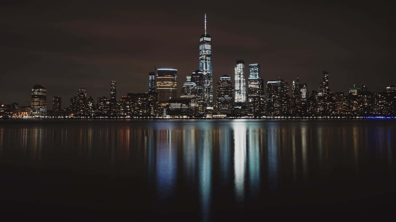 720p Ny City 桌布 壁紙 — 在黑暗天空下，紐約天際線倒映在平靜水面上，呈現出迷人的夜景。