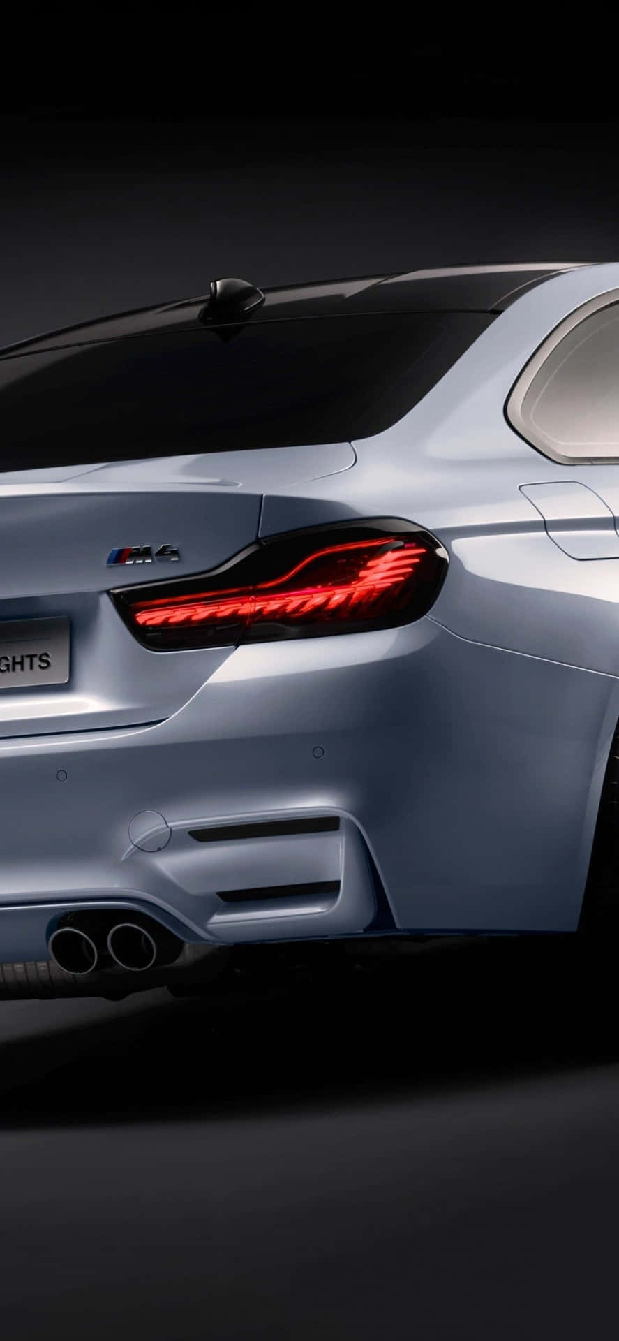 BMW 動圖 桌布 壁紙 — 在黑暗工作室背景下，一輛時尚的銀色寶馬M4雙門轎跑車後視圖，帶有發光的紅色尾燈和雙排氣管。
