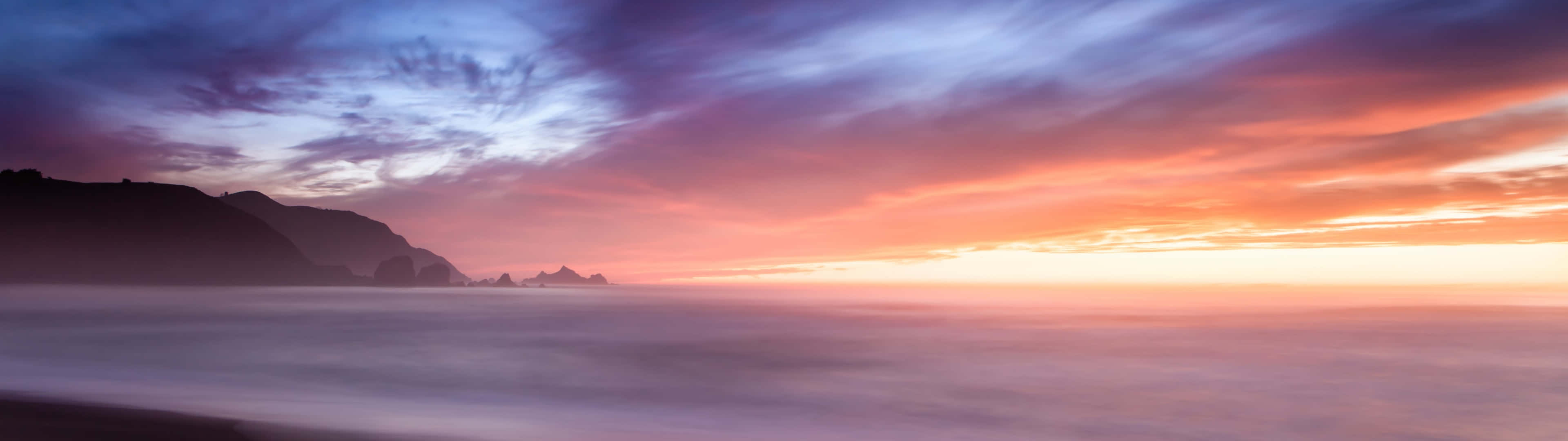 Beach Sunset HD 桌布 壁紙 — 在黑暗懸崖上，夕陽下長時間曝光的海景，水面平滑，天空呈現鮮豔的紫橙色。