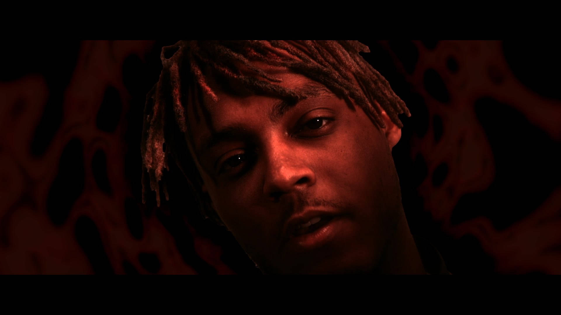 在黑暗抽象背景前，紅光照耀下留著辮子髮型的男子肖像。 — Juice Wrld 壁紙