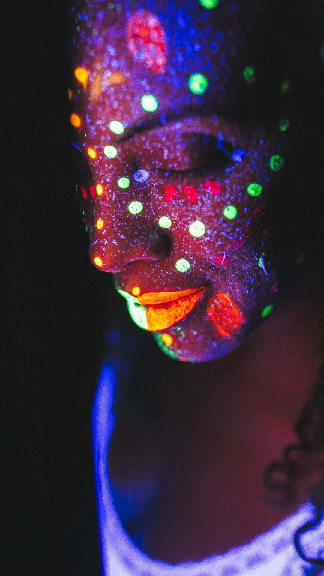 Glow In The Dark 桌布 壁紙 — 在黑暗環境中，黑光下一個人臉上閃爍著鮮豔的霓虹點的近距離特寫。