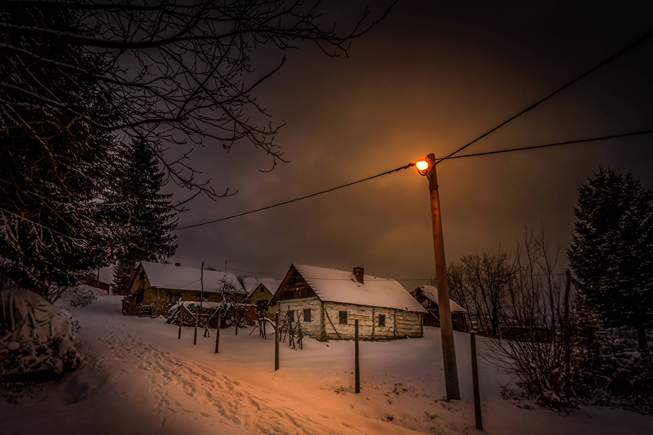 Winter House 桌布 壁紙 — 在黑暗的冬日天空下，一盞孤獨的路燈將溫暖的光芒灑在積雪覆蓋的小屋上。
