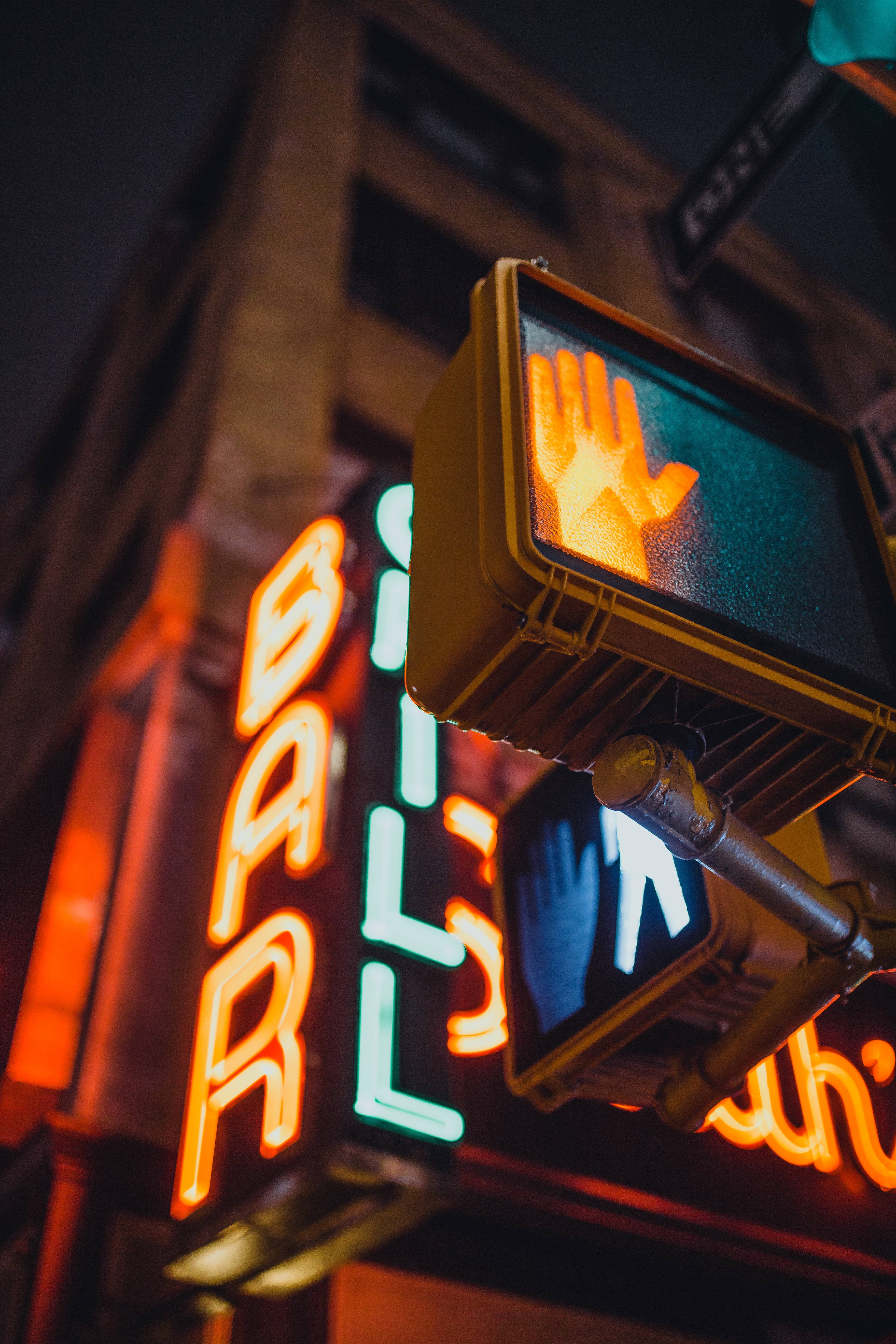 neon sign 桌布 壁紙 — 在黑暗的城市夜晚背景下，交通燈上發光的橙色手勢信號與霓虹燈酒吧招牌形成對比。