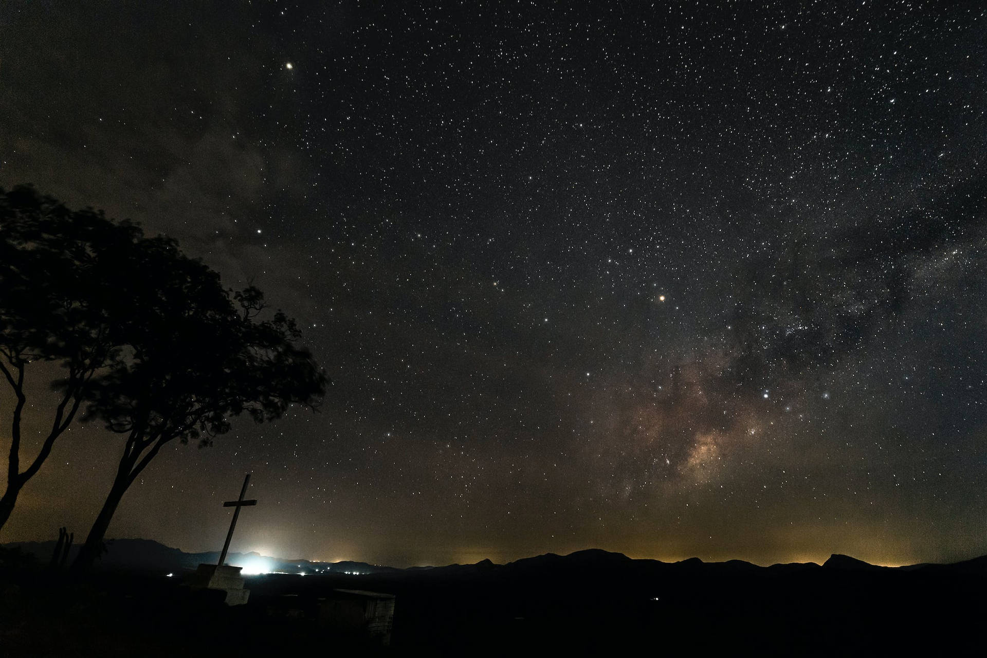 在可見銀河的星空夜空下的剪影樹木和十字架。