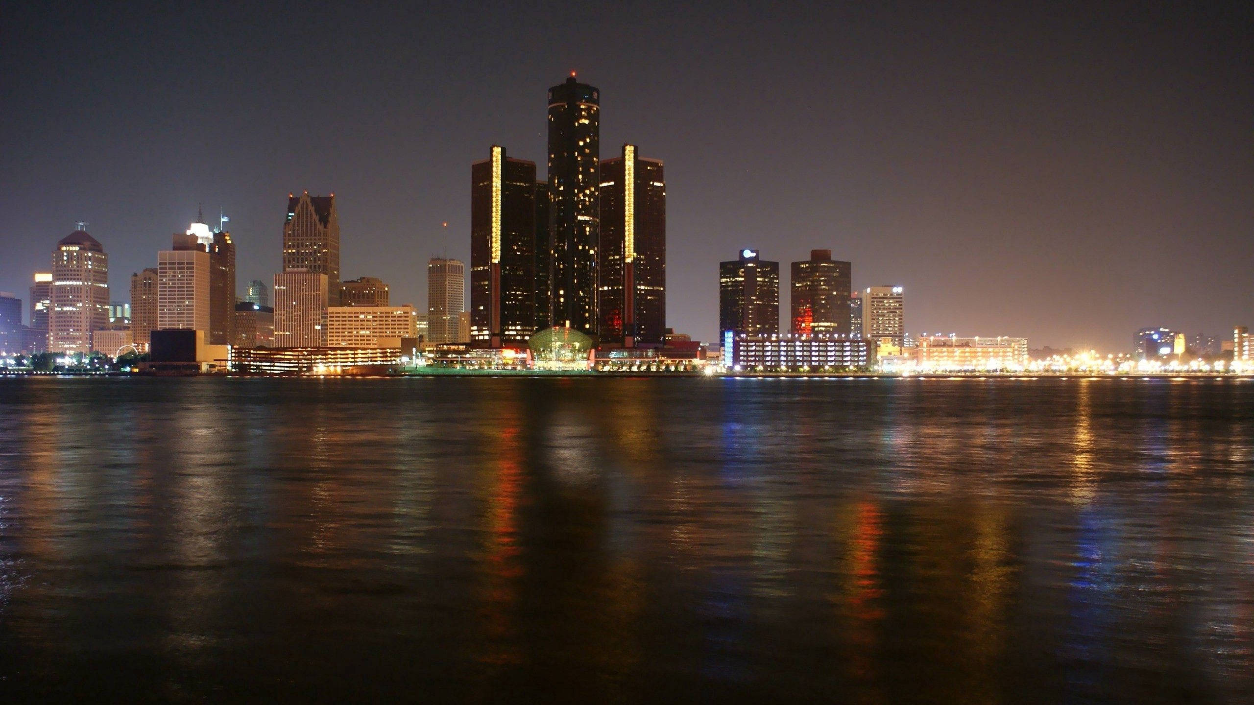 detroit 桌布 壁紙 — 在黑暗的天空下，明亮的摩天大樓倒映在平靜水面上的充滿活力的夜景。