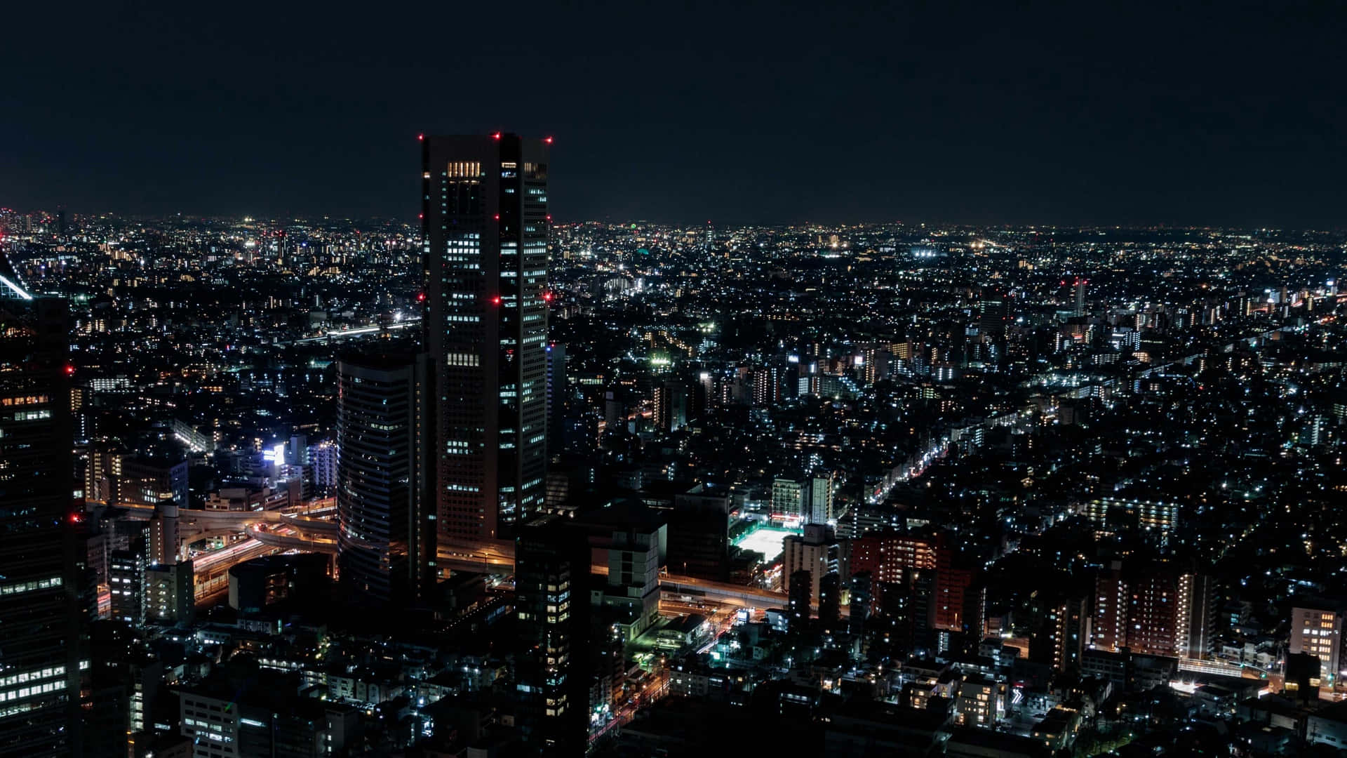 City Night 桌布 壁紙 — 在黑暗的天空下，無數發光的窗戶和街燈照亮了廣闊的城市景觀的鳥瞰夜景。
