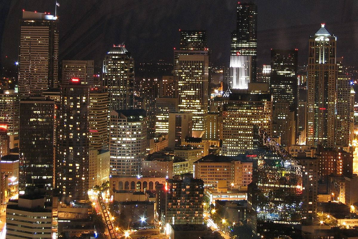 Seattle Skyline 桌布 壁紙 — 在黑暗的天空映襯下，高聳的摩天大樓閃爍著溫暖的金色和白色燈光，構成令人目眩的夜景。