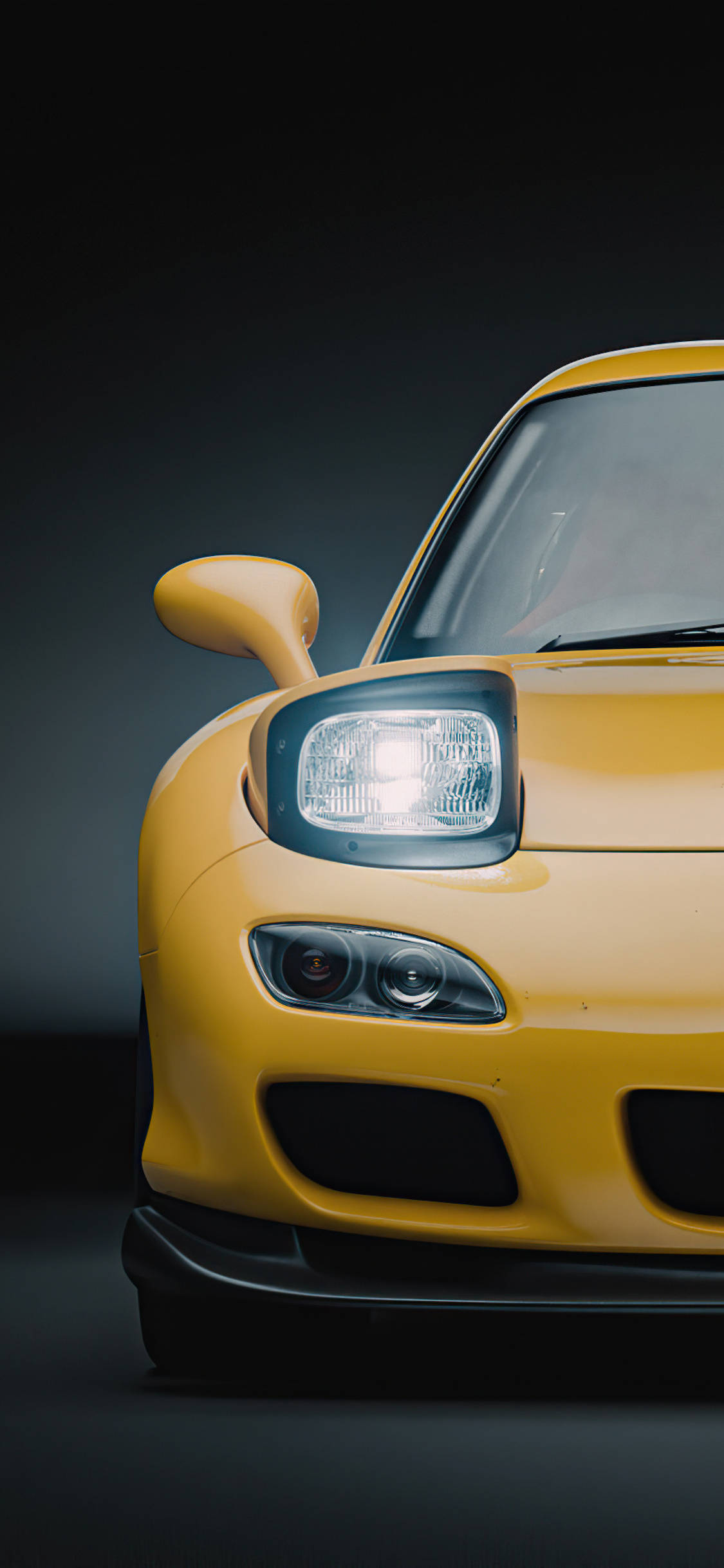 Rx7 iPhone 桌布 壁紙 — 在黑暗的攝影棚背景下，一輛充滿活力的黃色跑車前端特寫，帶有發光的頭燈。
