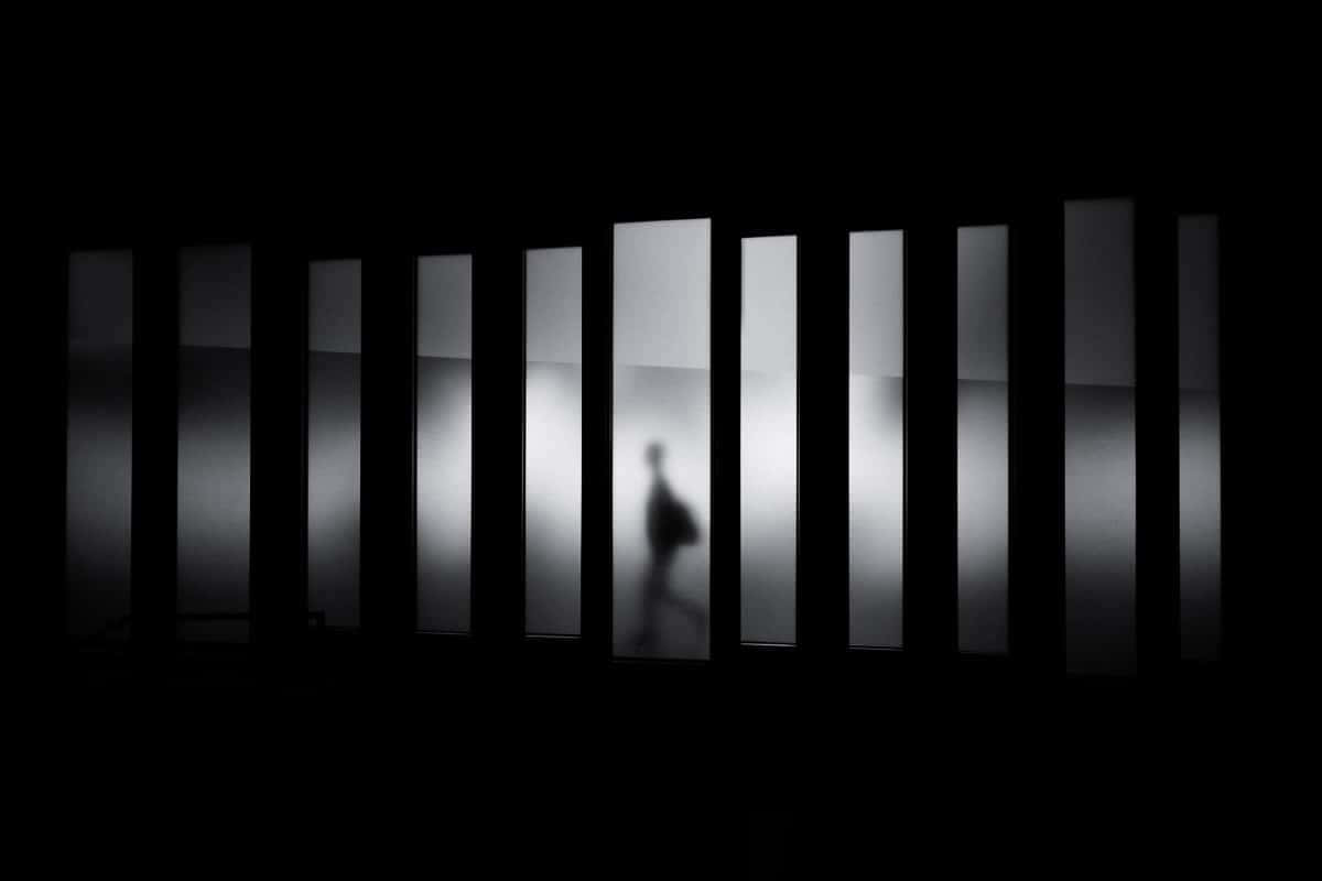 Black And White Architecture 桌布 壁紙 — 在黑暗的走廊中，一個模糊的人影穿過一排垂直的磨砂玻璃板。