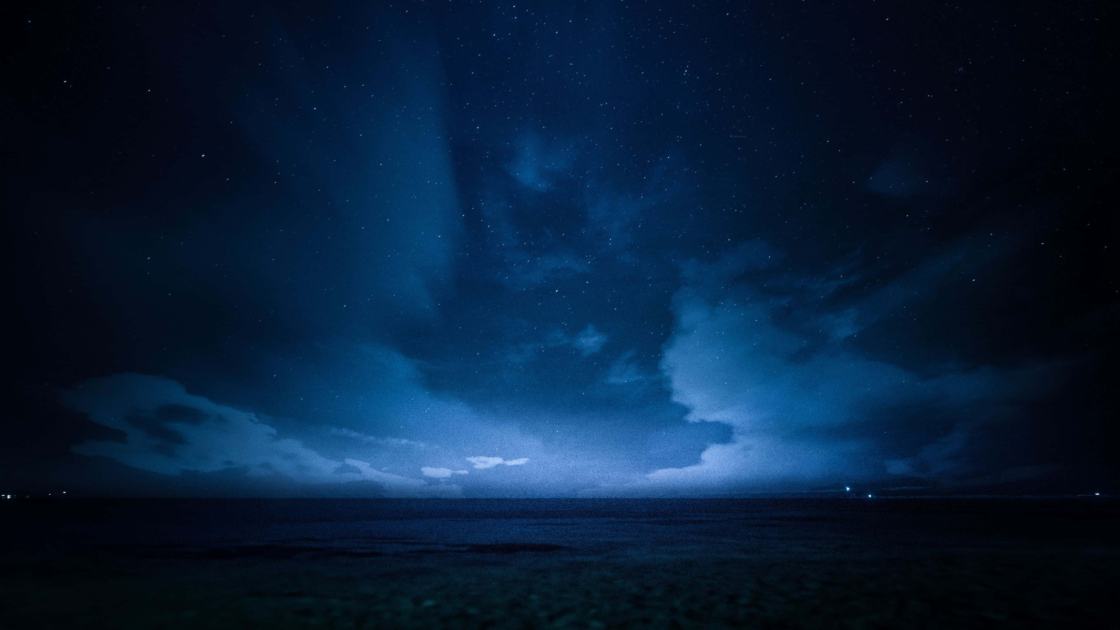 Dark Sky 桌布 壁紙 — 在黑暗的雲層下，閃爍的藍色極光在平靜的海洋上空舞動，星空燦爛。