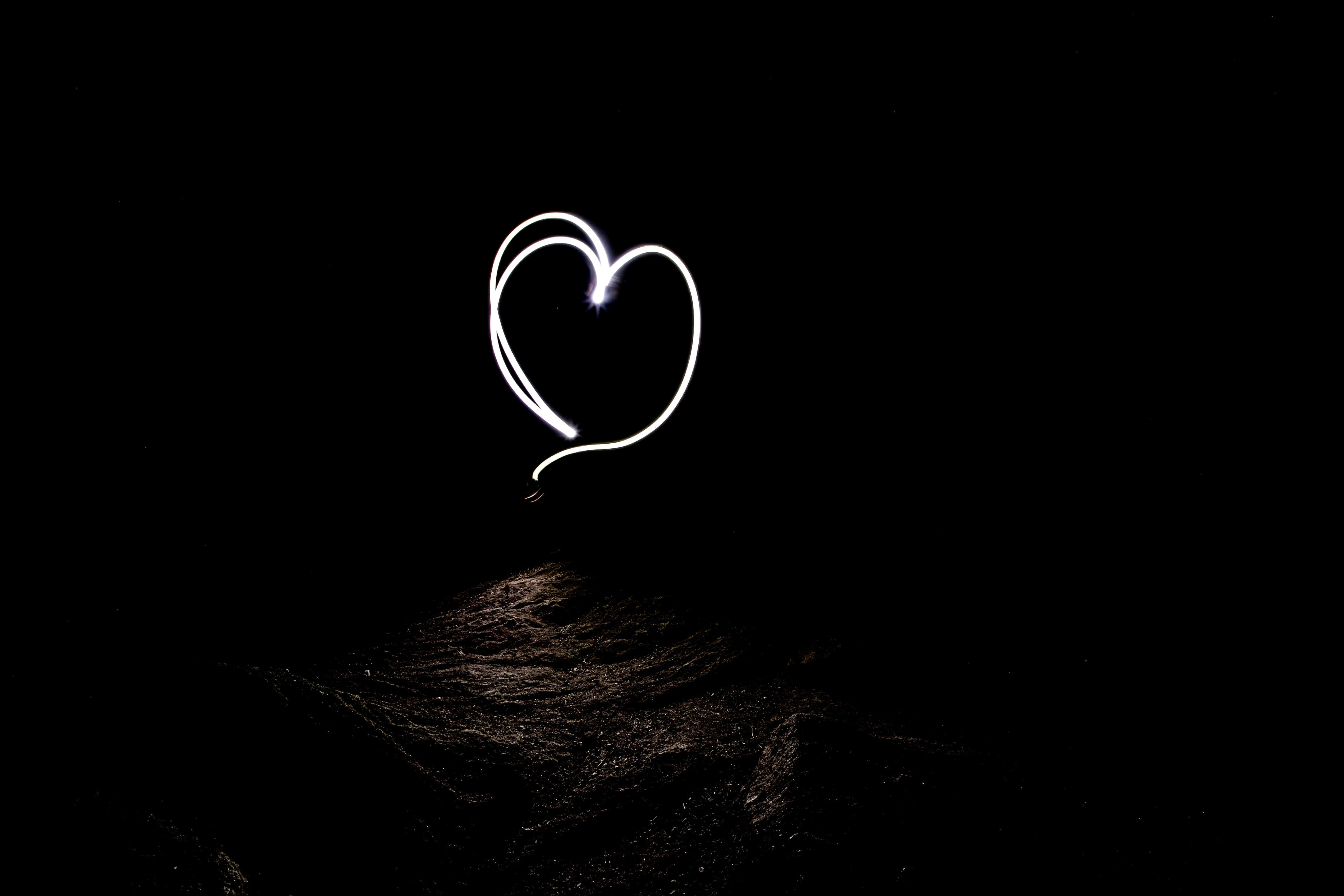 Black And White Heart 桌布 壁紙 — 在黑暗紋理的地面上，漆黑夜空中由光跡形成的發光白色心形。
