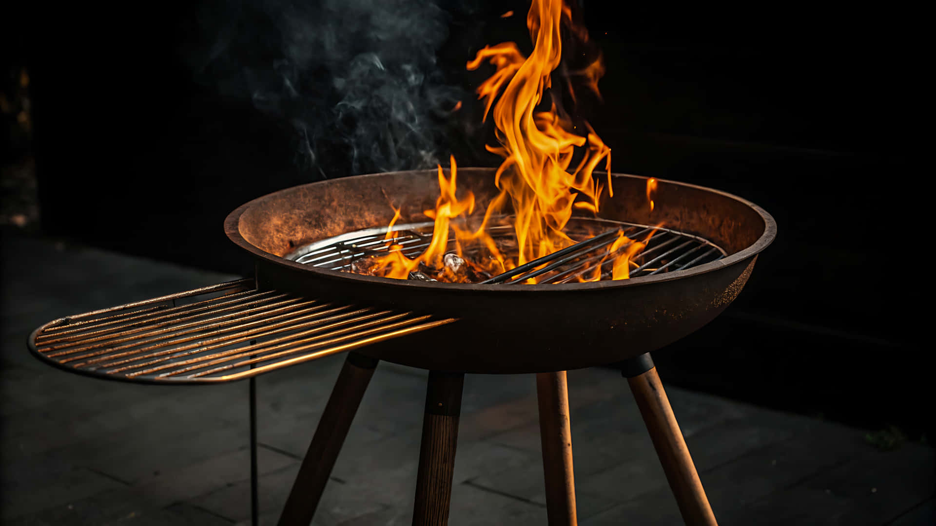 Barbecue grill with flames and smoke rising against a dark background 壁紙 — 在黑暗背景下，一個帶木腿的生鏽圓形烤架迸發出鮮豔的橙色火焰。