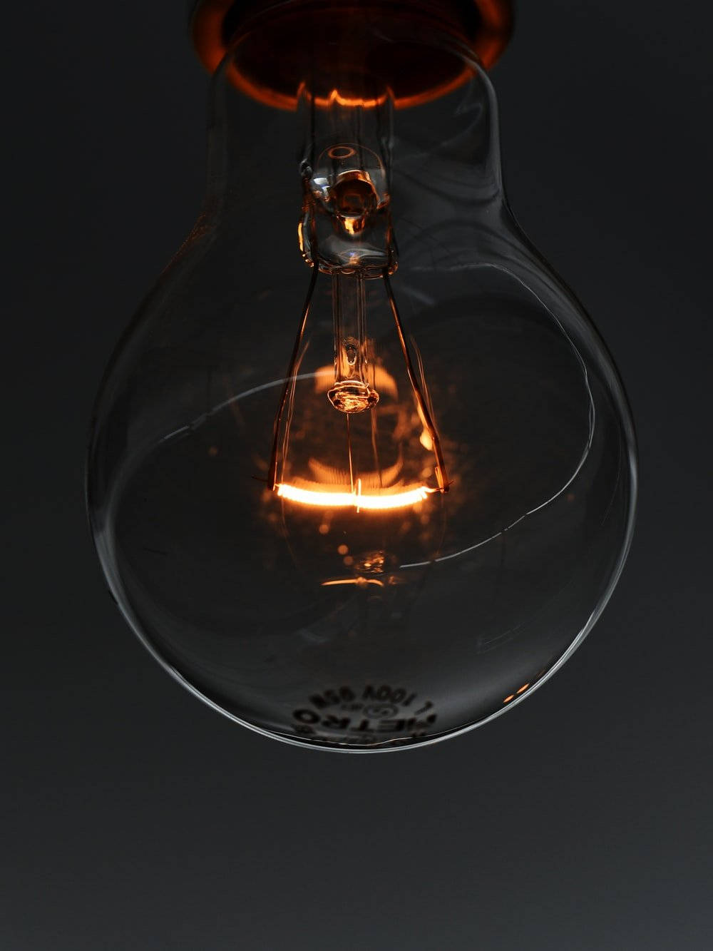 電力 桌布 壁紙 — 在黑暗背景下，一盞發光的復古白熾燈泡散發出溫暖的燈絲光。