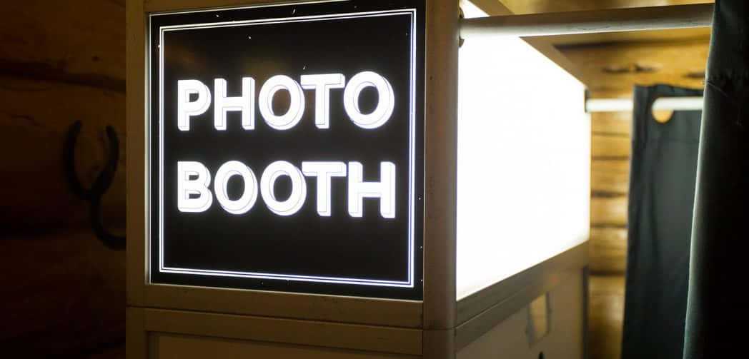 Photobooth 桌布 壁紙 — 在黑暗背景的鄉村風格木房間內，一個發光的霓虹燈牌，以粗體白色字母顯示PHOTO BOOTH。