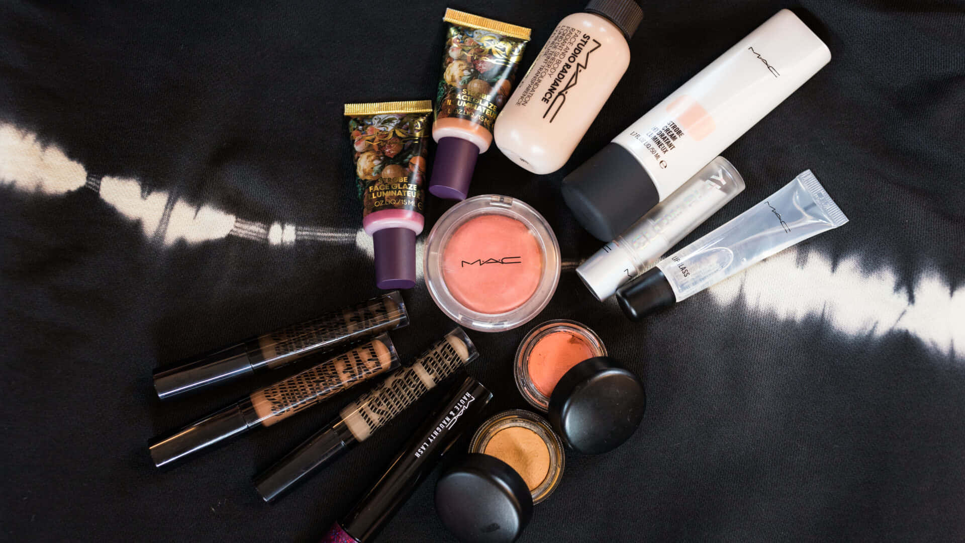 Mac Cosmetics 桌布 壁紙 — 在黑白紮染布料背景上排列的MAC化妝品平鋪圖。