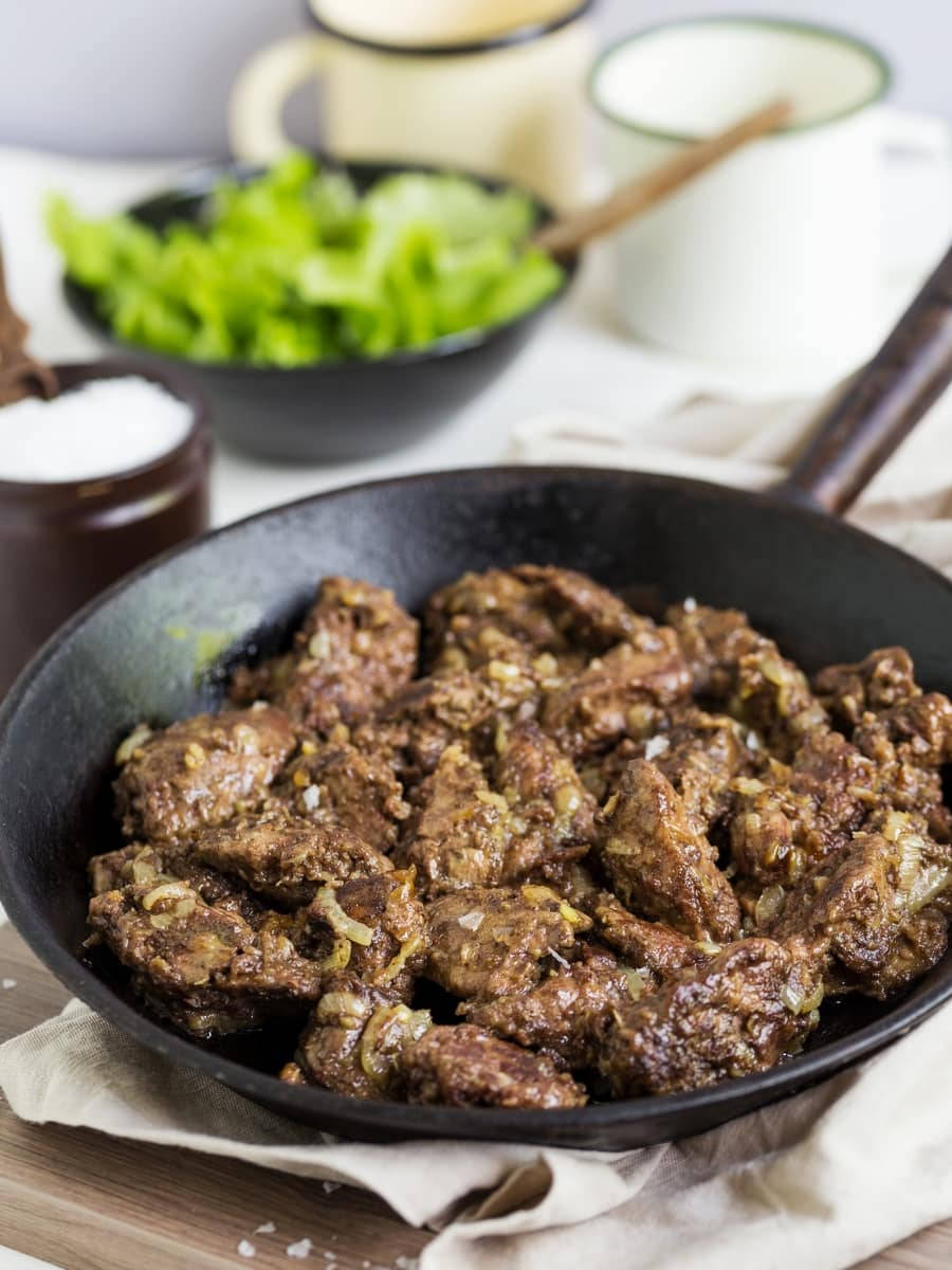 meat 桌布 壁紙 — 在黑色鑄鐵煎鍋中滋滋作響的調味肉塊，配以新鮮生菜和搪瓷杯，背景柔和。