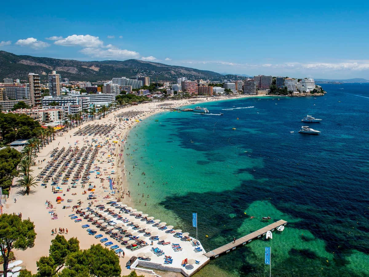 Spanish Beach 桌布 壁紙 — 地中海繁忙海灘的鳥瞰圖，碧綠海水擠滿曬太陽的人和遊艇，鄰近沿海城市。