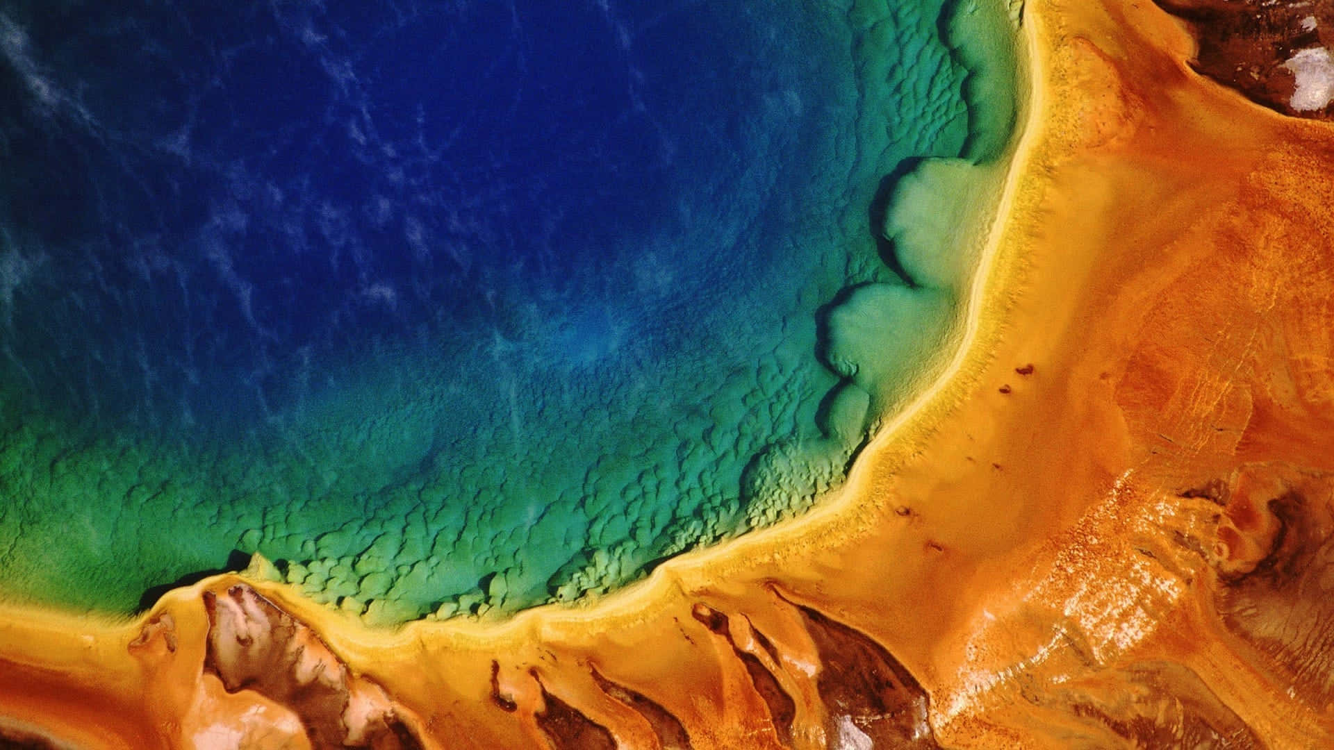 Yellowstone 桌布 壁紙 — 地熱池的鳥瞰圖，鮮豔的藍綠色水域與金橙色富含礦物質的邊緣交匯。